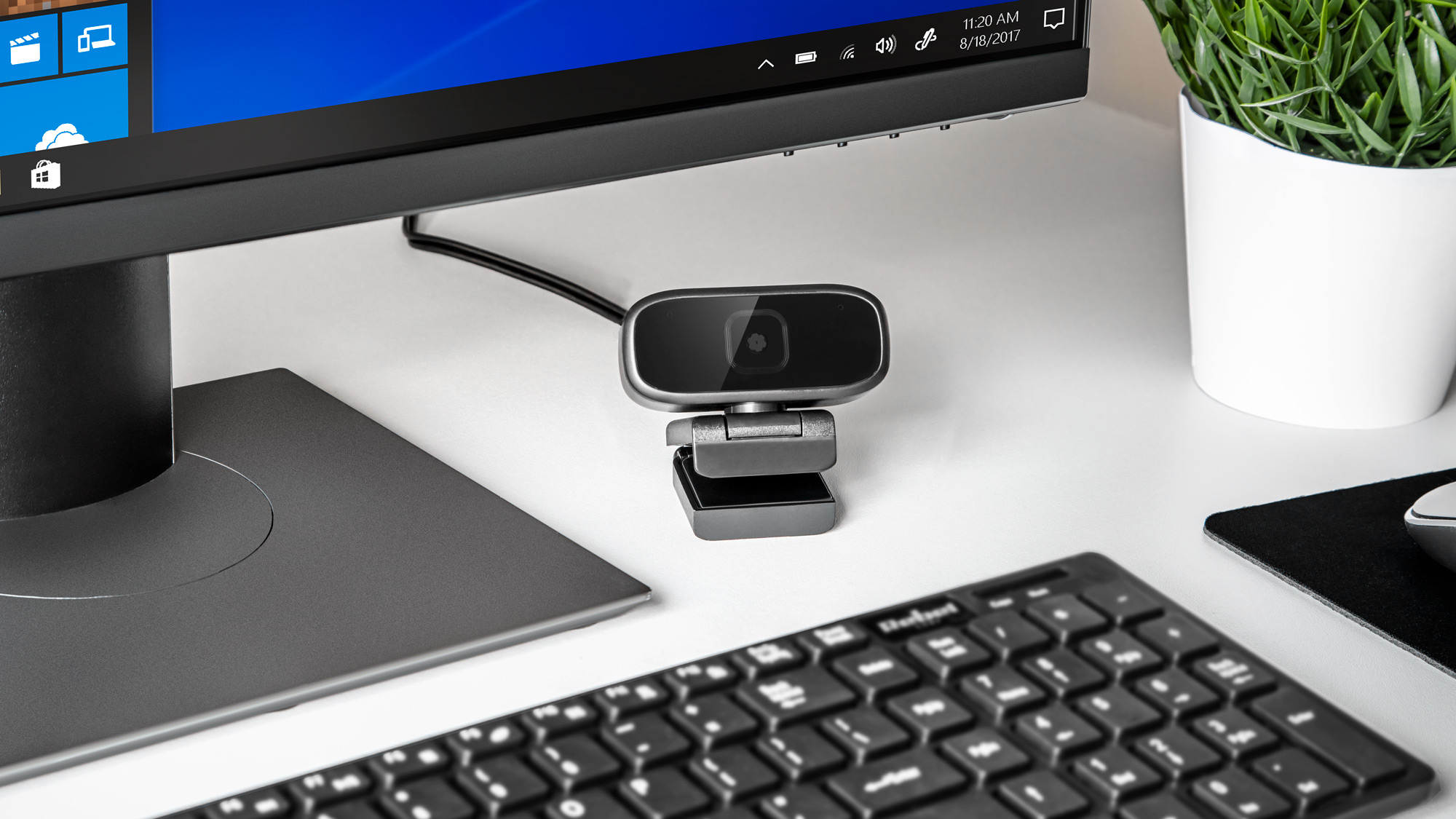 Mała czarna kamera internetowa stoi na białym biurku przed monitorem.
