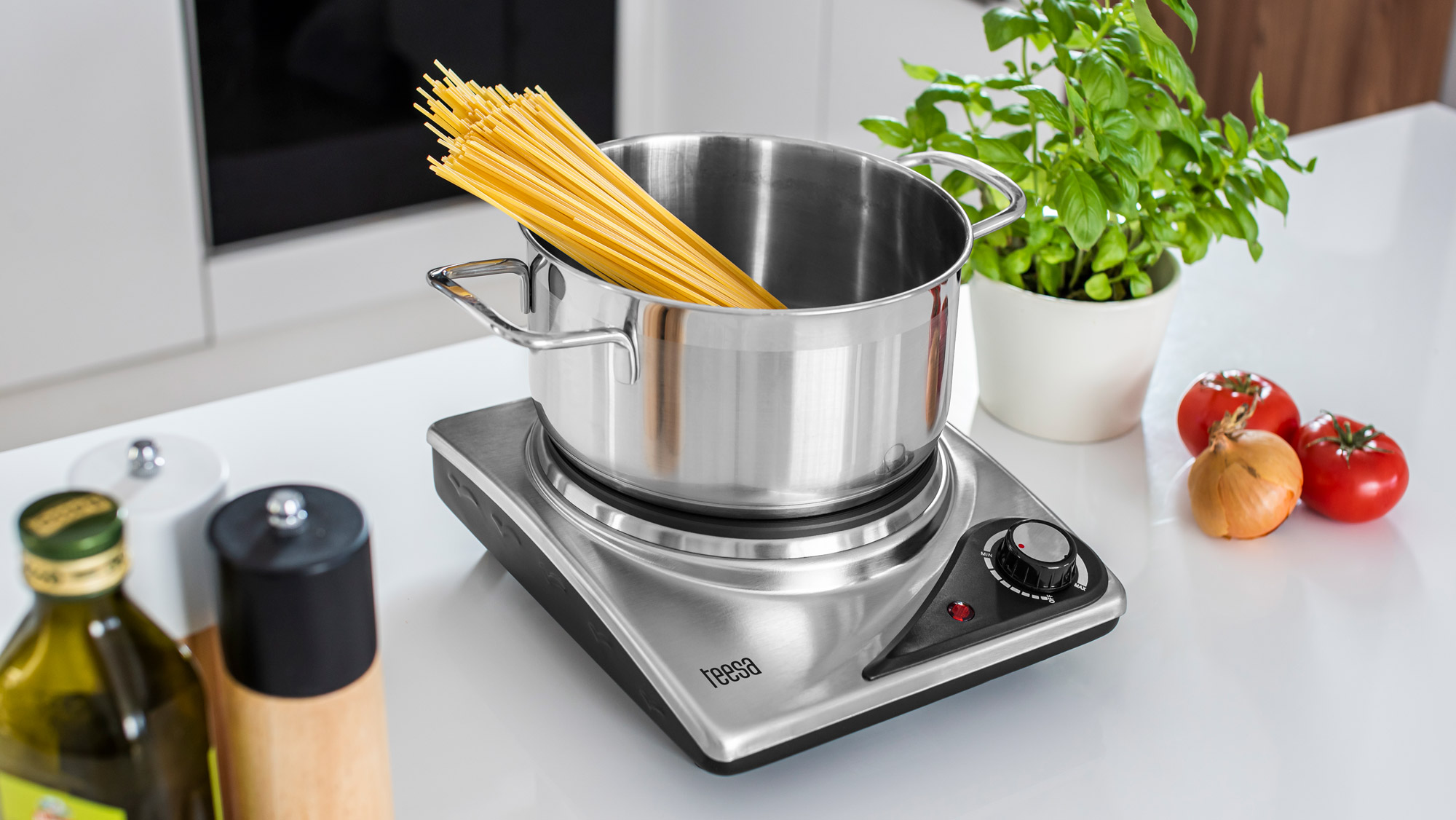 Garnek ze stali nierdzewnej z surowym spaghetti stoi na elektrycznej płycie grzewczej.