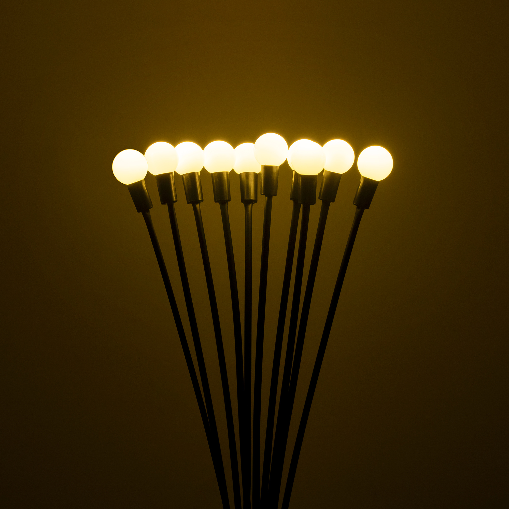 Dziewięć podświetlonych okrągłych lamp na długich, cienkich czarnych prętach na żółtym tle.