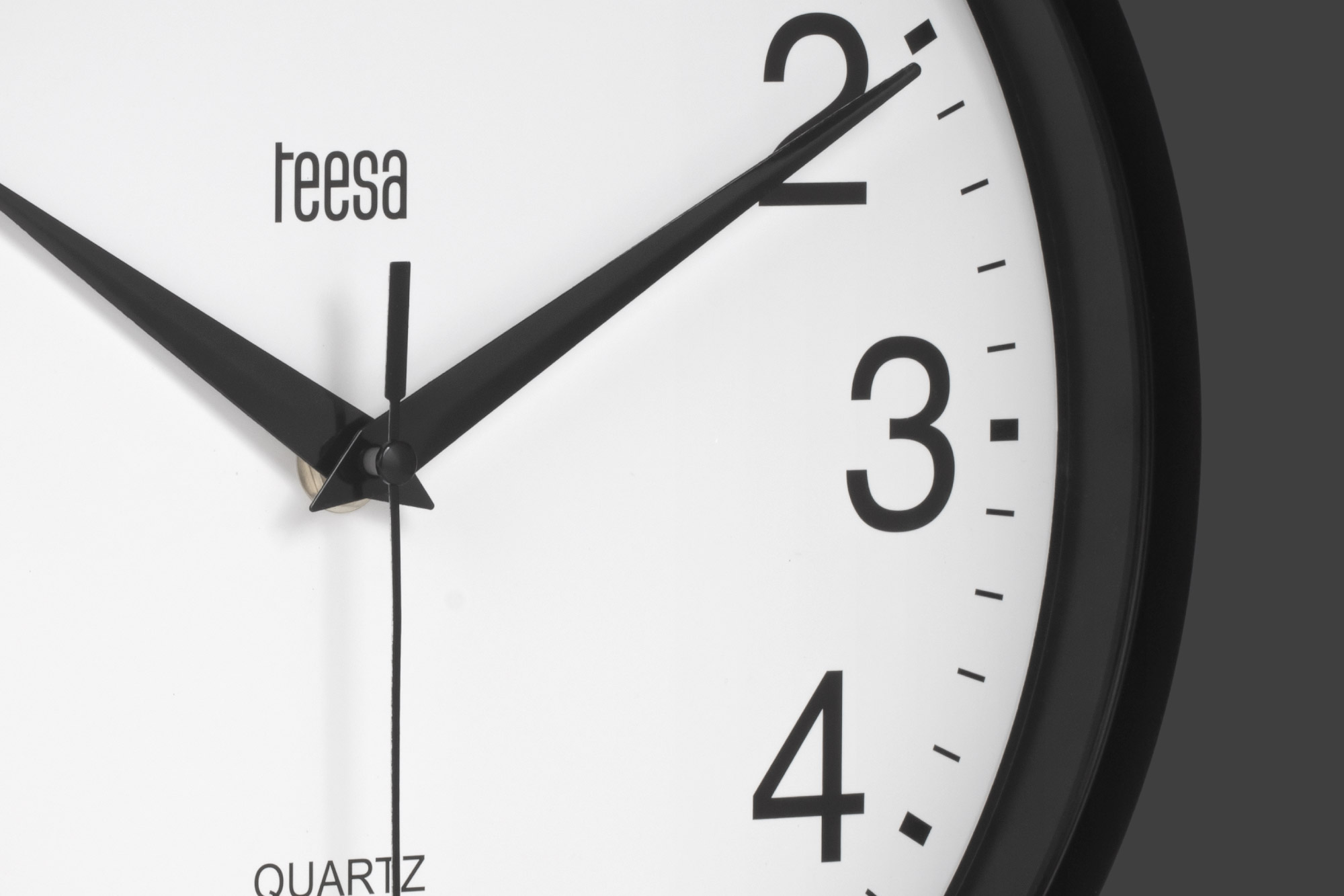Zbliżenie białego zegara ściennego z czarnymi cyframi i wskazówkami, logo Teesa i napisem quartz.