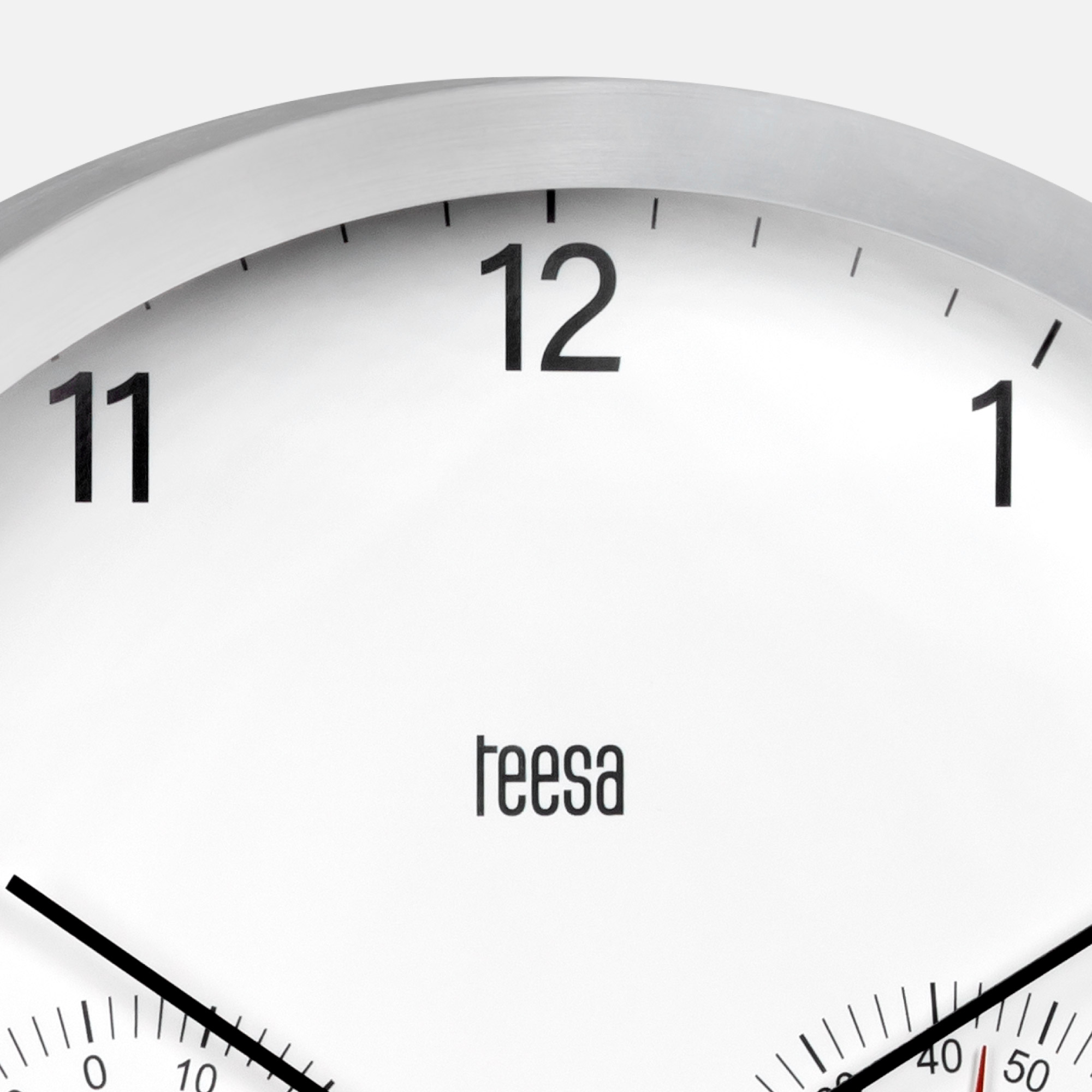 Zbliżenie tarczy zegara ściennego Teesa z cyframi 11, 12 i 1 oraz dwiema mniejszymi tarczami.