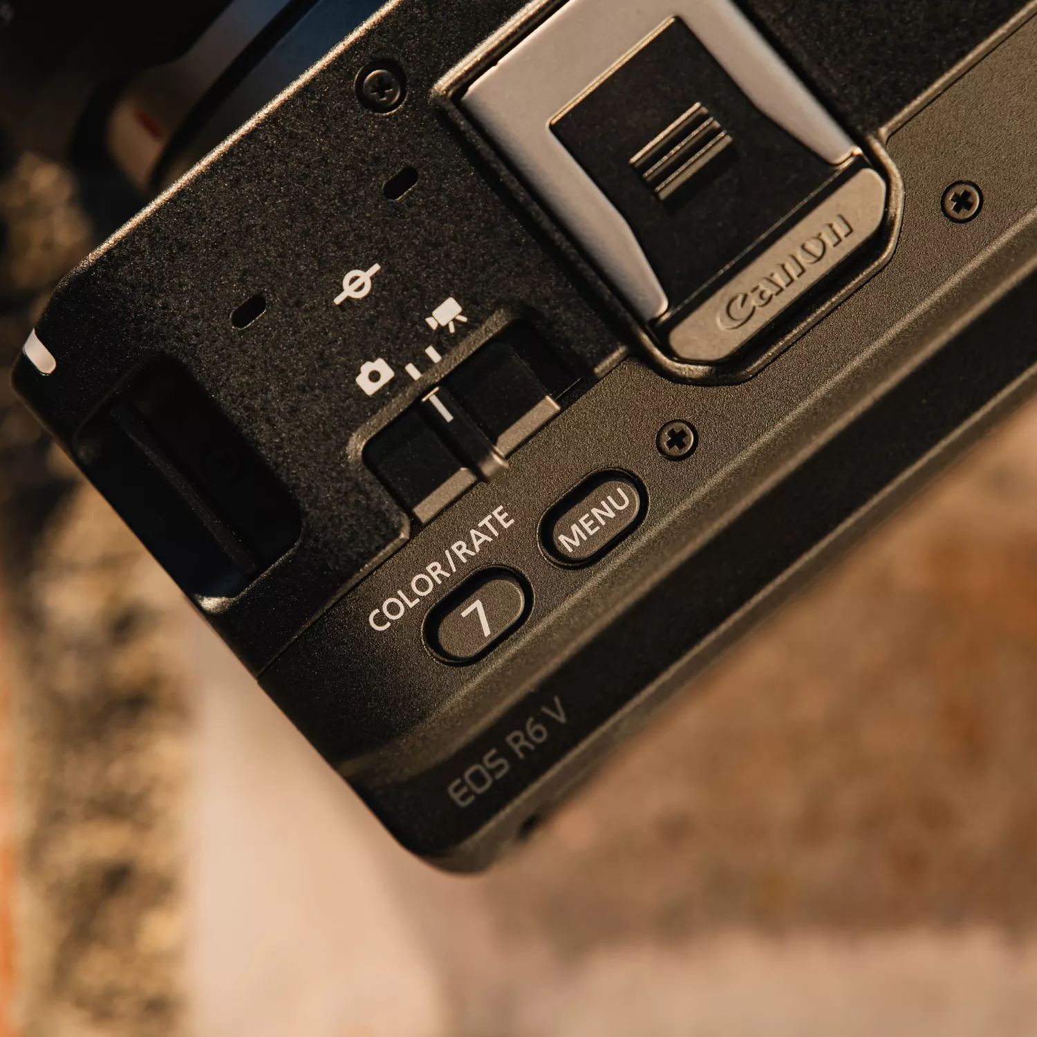 Vista superior de un cuerpo de cámara negro Canon EOS R6 V que muestra botones, zapata y texto del modelo con luz cálida.