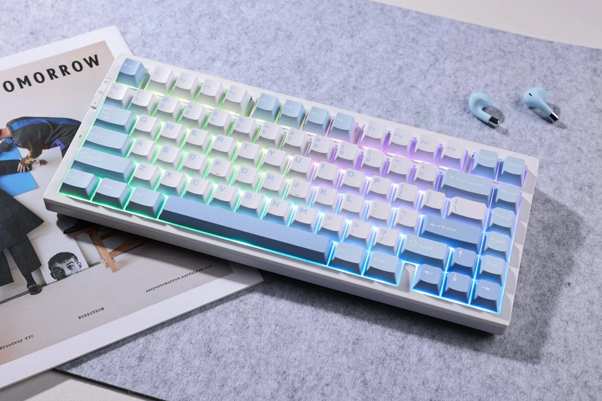 Kulaklık ve derginin yanında gri bir mat üzerinde RGB arka aydınlatmalı beyaz ve mavi mekanik klavye.