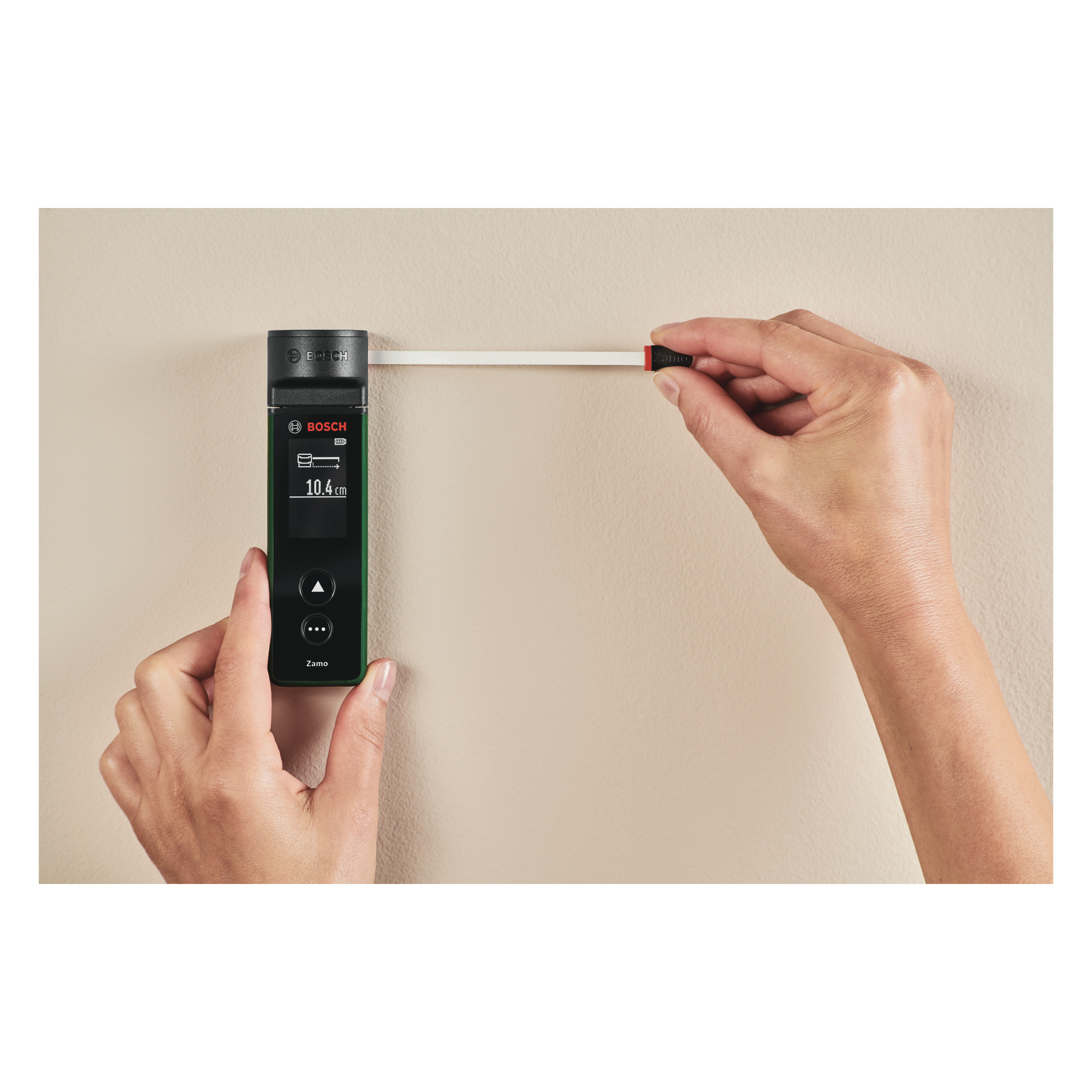 Person misst eine Wand mit einem digitalen Bosch-Laser-Entfernungsmesser und einem Maßbandaufsatz.