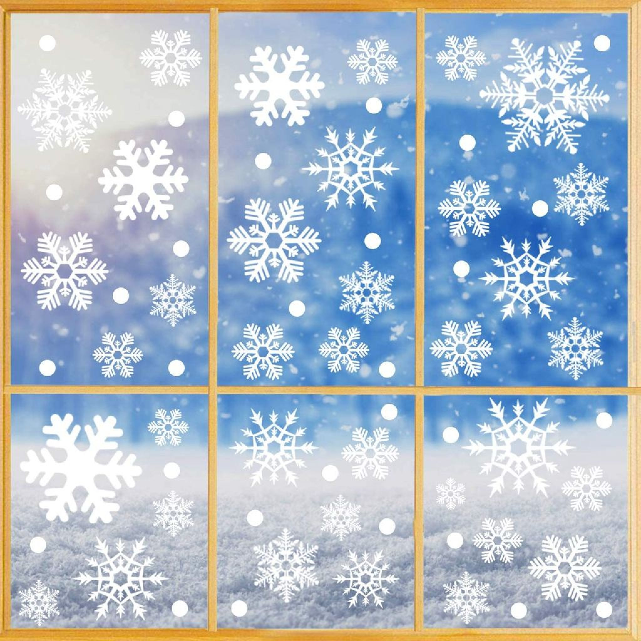 Weiße Schneeflockenaufkleber und Punkte auf einem Fenster mit verschneiter Winterlandschaft im Hintergrund.