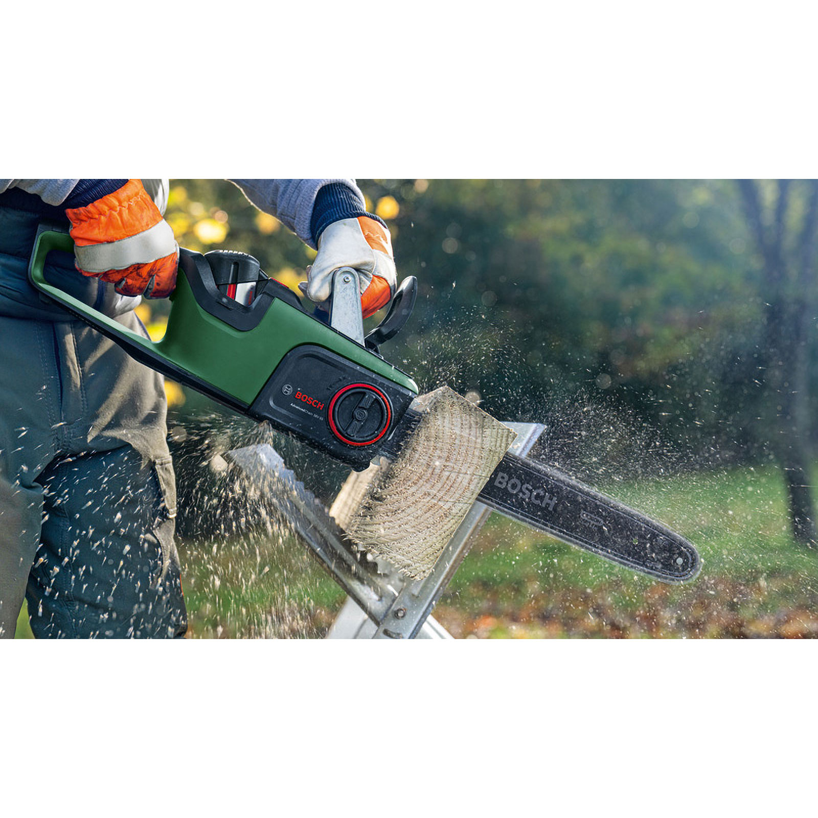Person schneidet Holzstueck mit gruener Bosch Kettensäge im Garten, Holzspäne fliegen umher.