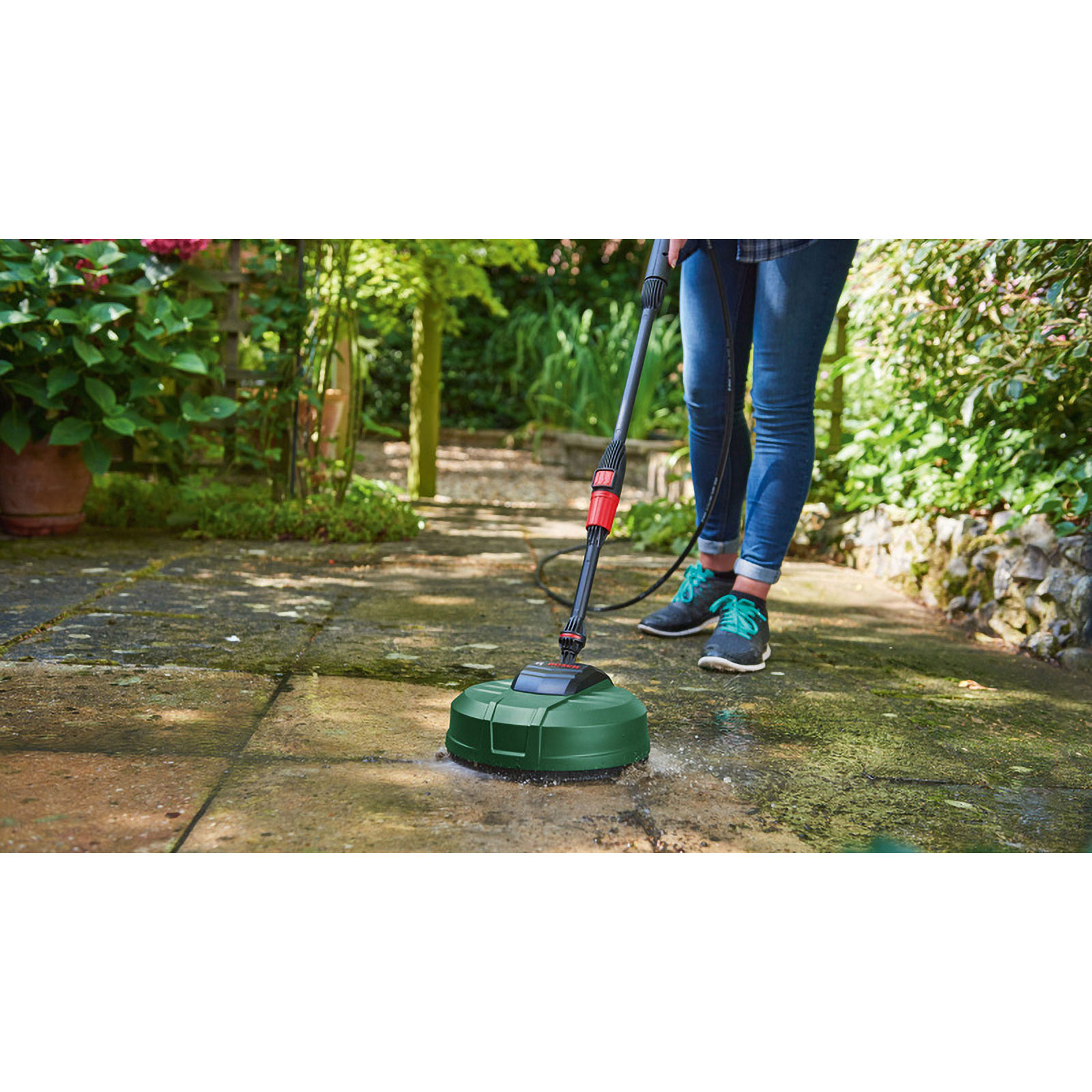 Eine Person reinigt eine Steinterrasse mit einem grünen Hochdruckreiniger im Garten.