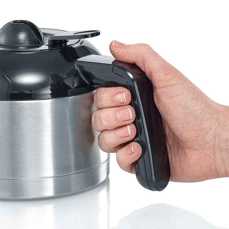 Una mano tiene il manico nero di una caffettiera in acciaio inossidabile e plastica nera.