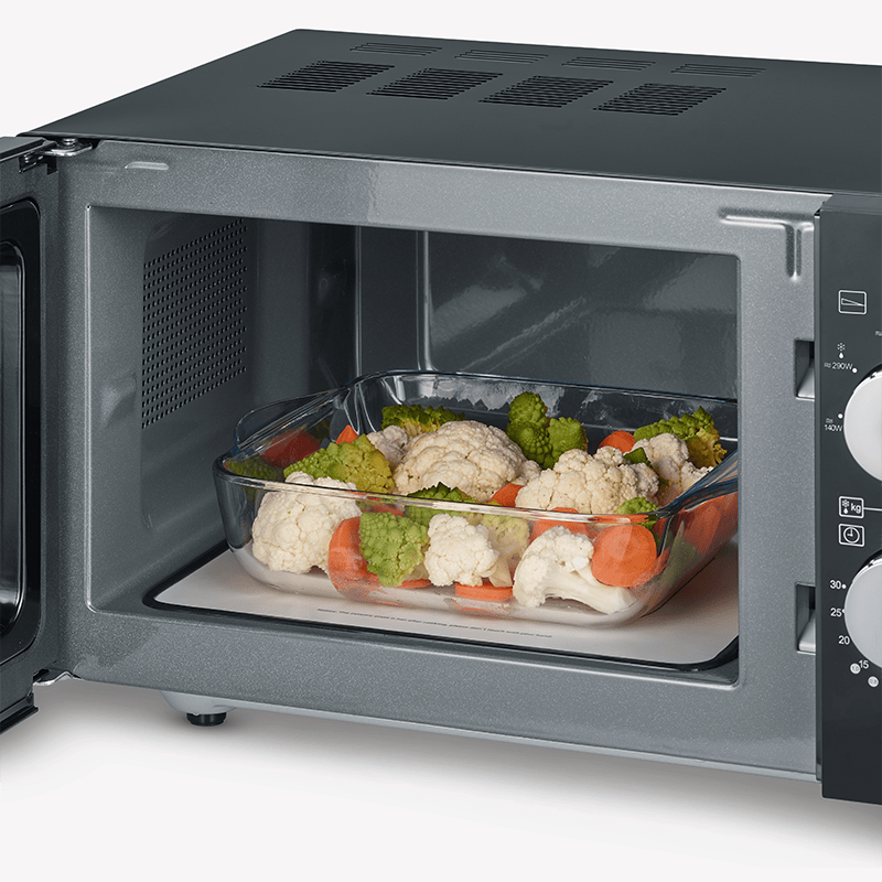 Plat en verre avec chou-fleur, brocoli et carottes dans un micro-ondes ouvert.