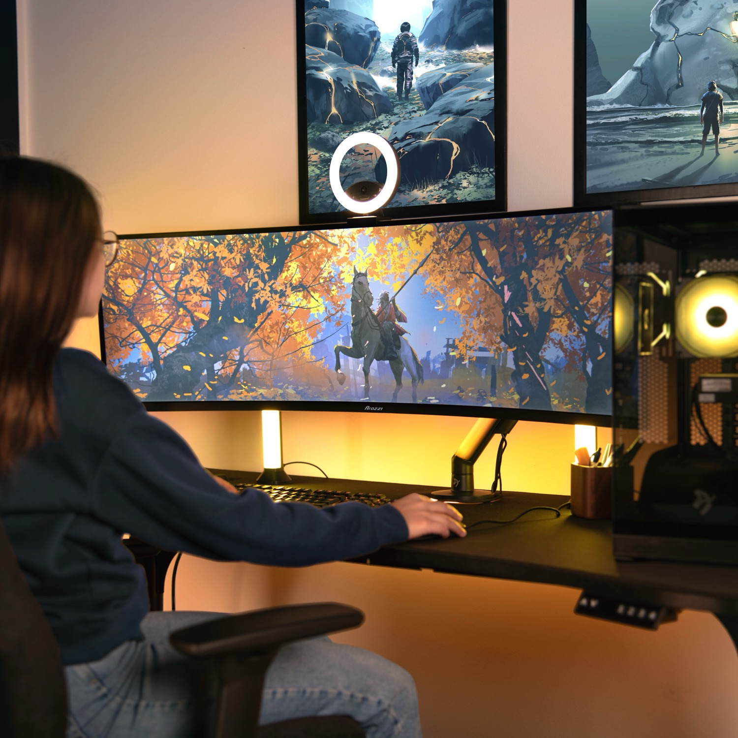 Eine Frau sitzt an einem Schreibtisch vor einem breiten Monitor, auf dem ein herbstliches Reiterbild zu sehen ist.