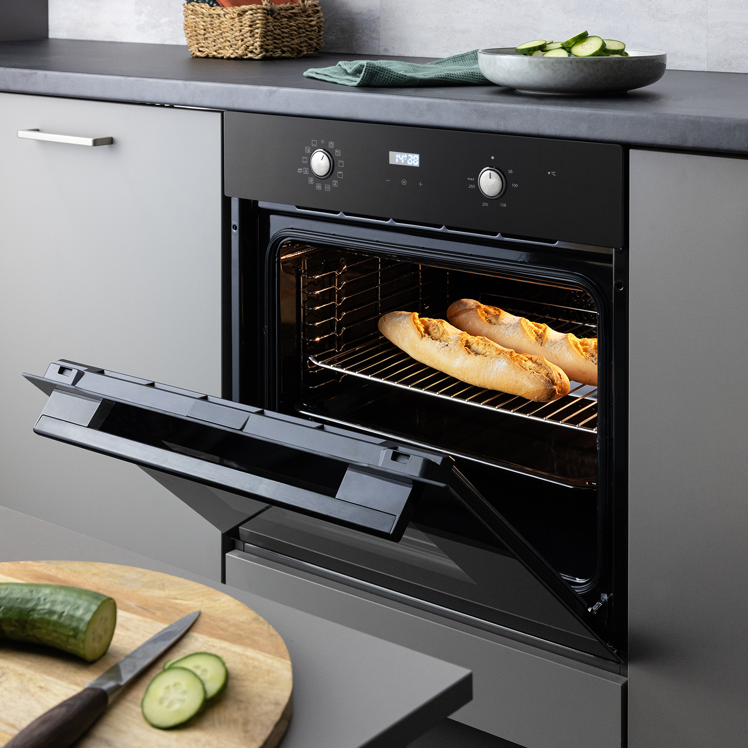 Ein offener Einbauofen zeigt zwei frisch gebackene Baguettes auf dem Rost, in einer modernen Küche mit Gurkenscheiben.