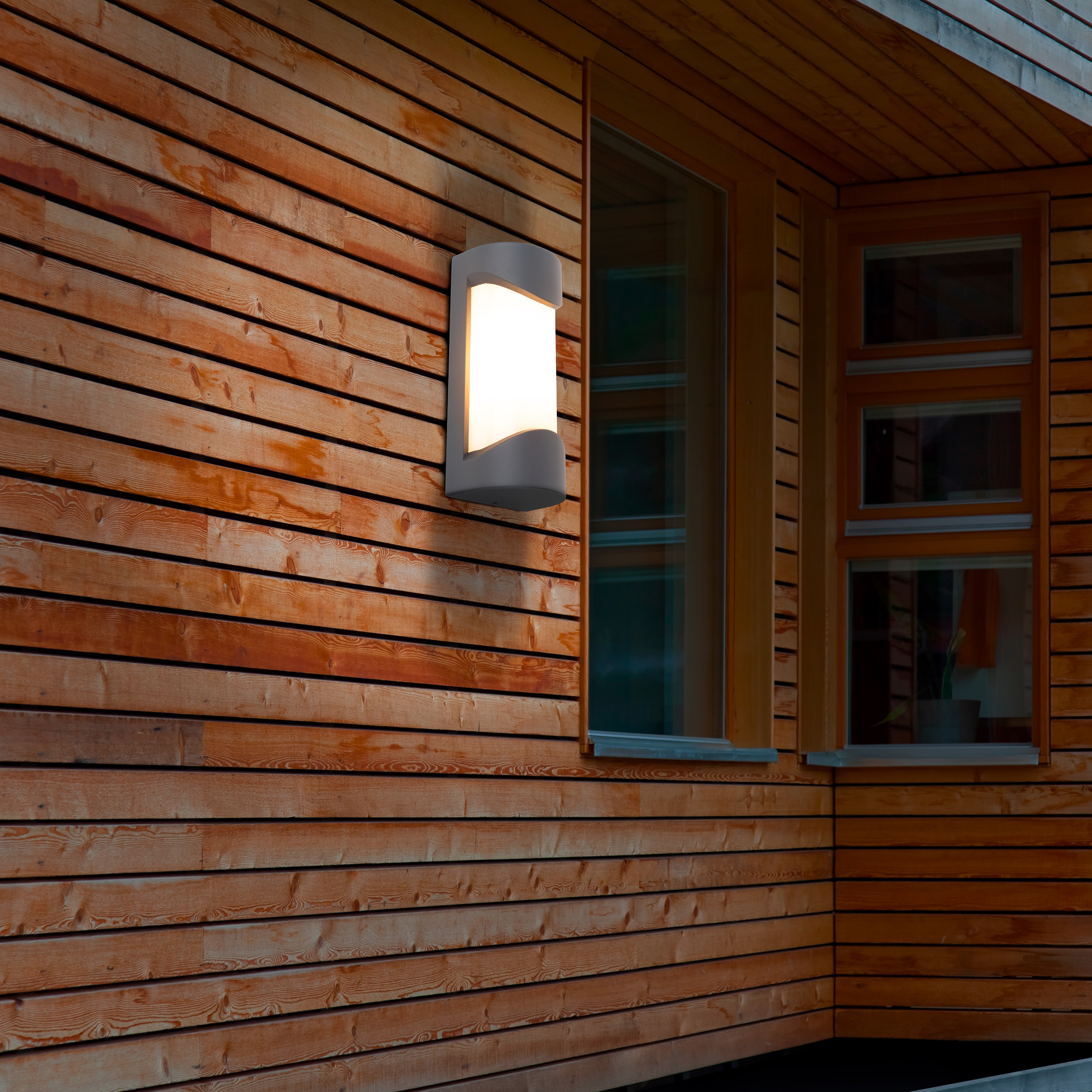 Eine beleuchtete Wandlampe an einer modernen Holzwand mit großen Fenstern.