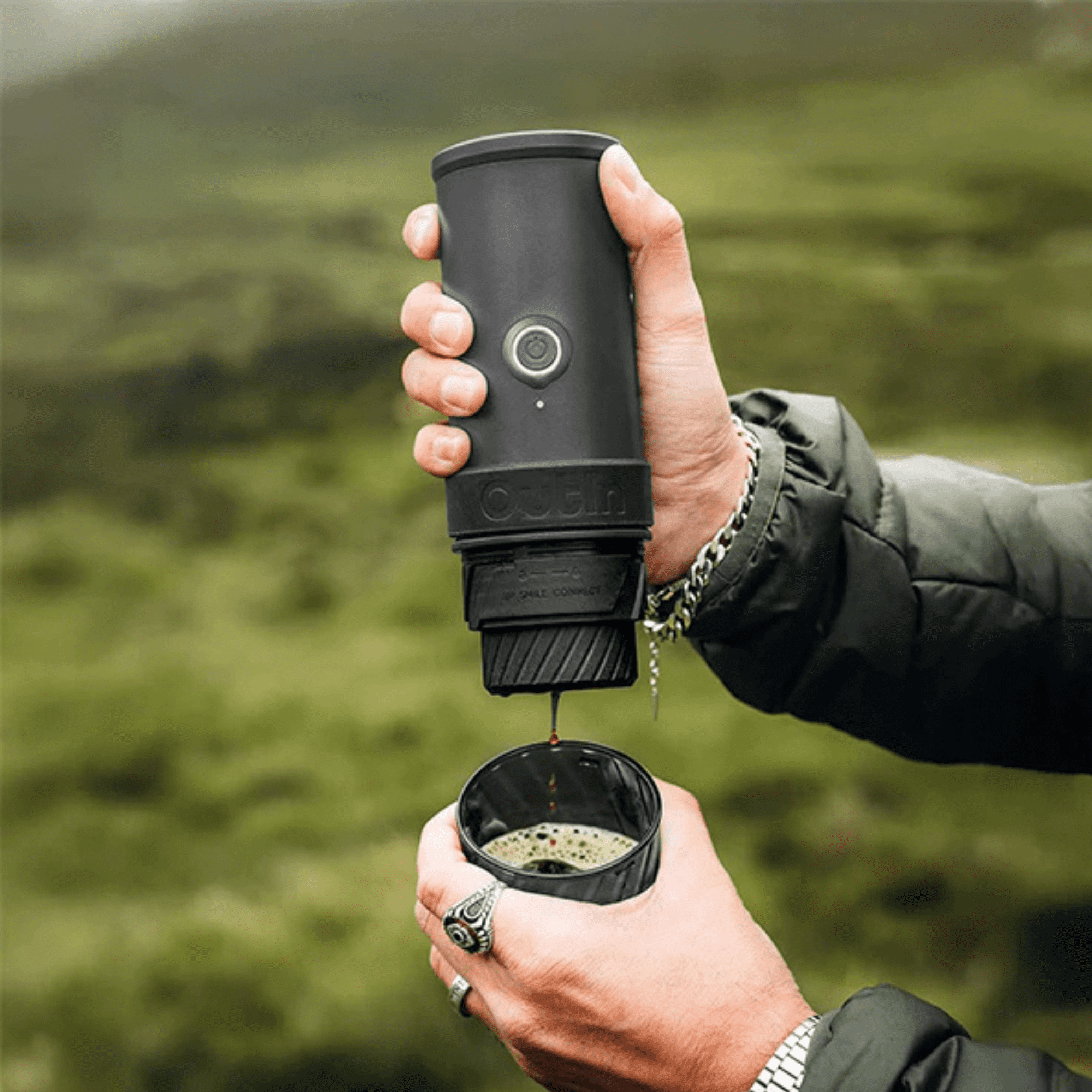 Una persona tiene una caffettiera nera e versa caffè in una tazza con sfondo verde.