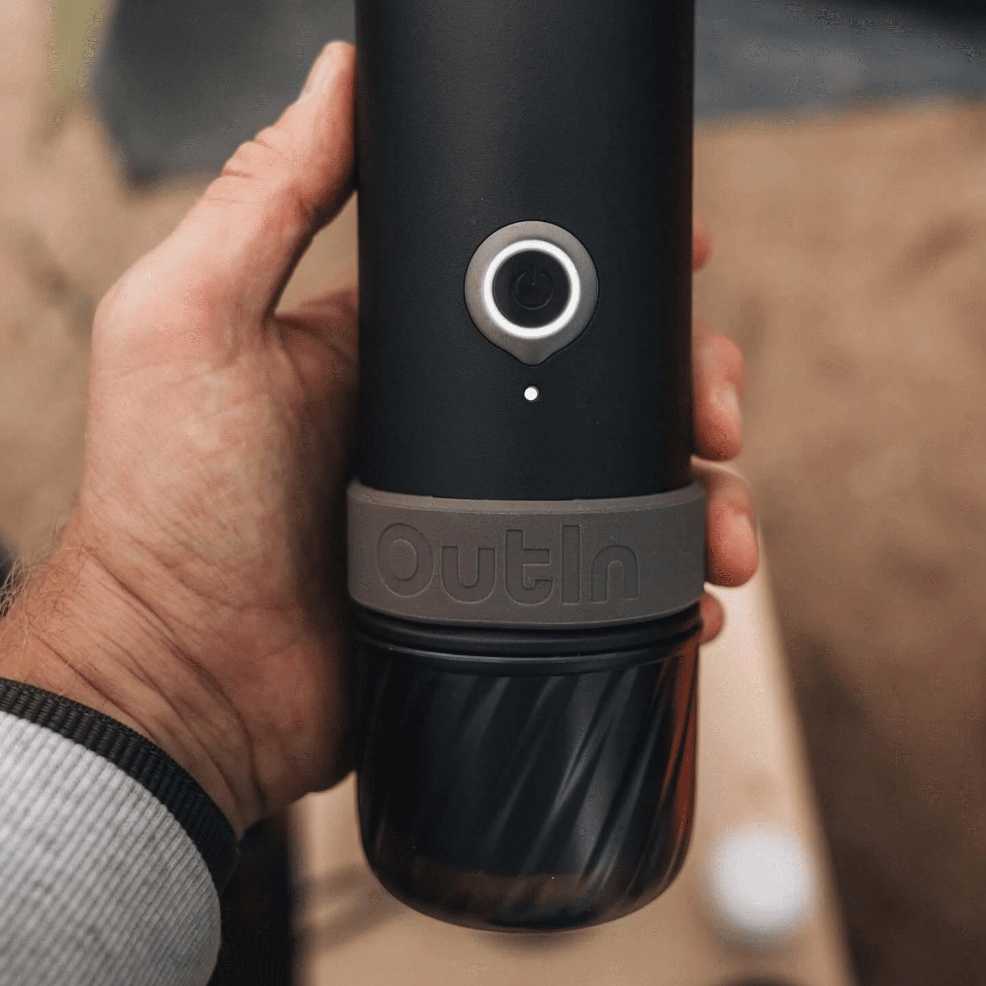 Una mano tiene una caffettiera nera Outin con un pulsante di accensione luminoso e base scanalata.