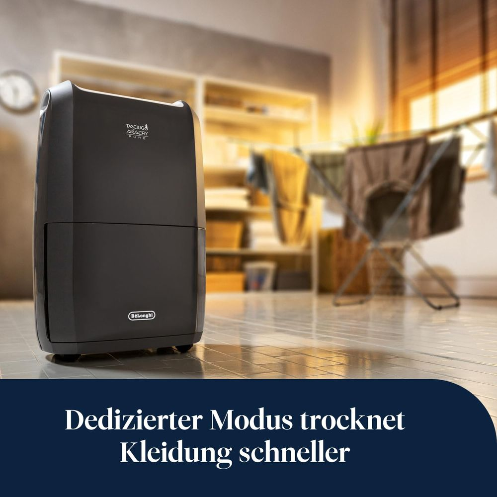 Un deshumidificador DeLonghi gris oscuro sobre suelo de baldosas con un tendedero al fondo.