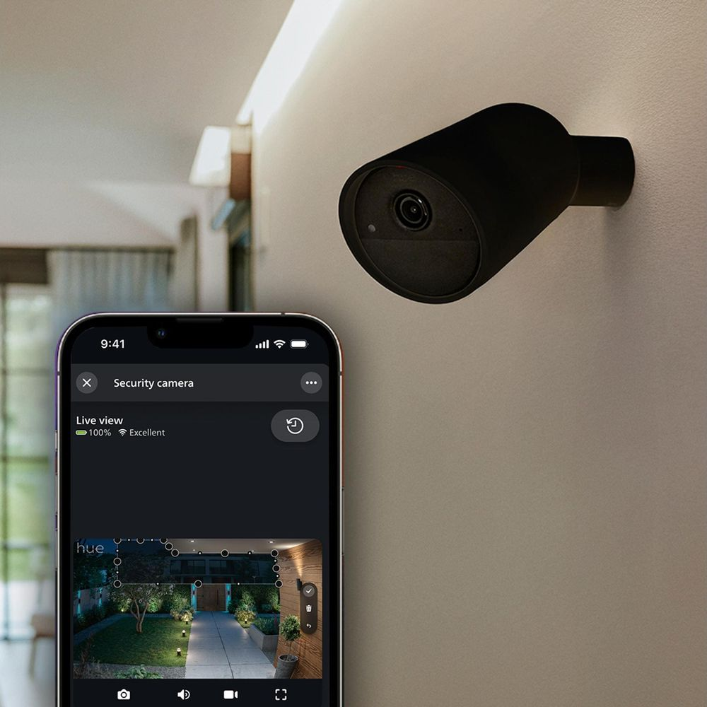 Eine schwarze Überwachungskamera an einer Wand und ein Smartphone, das ein Live-Bild anzeigt.
