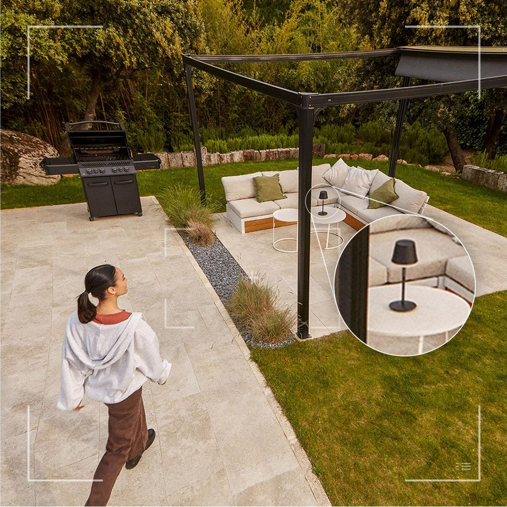 Eine Frau geht auf einer Terrasse mit Pergola, Lounge-Möbeln, Grill und einer Detailaufnahme einer Tischlampe.