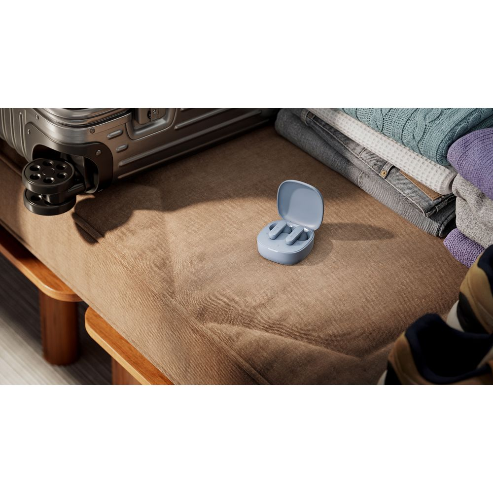 Una custodia per auricolari wireless azzurra poggia su una superficie marrone vicino a bagagli, vestiti e scarpe.