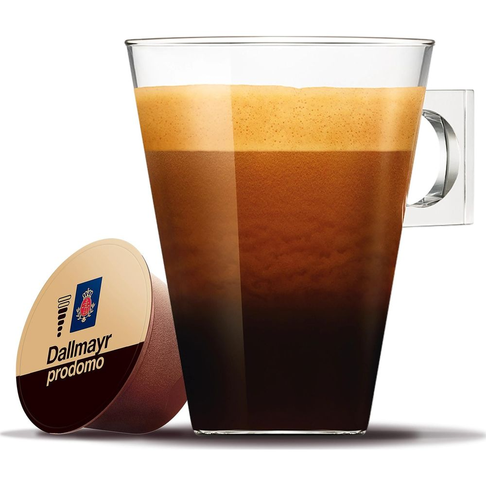 Eine Glastasse mit frisch gebrühtem Kaffee und goldener Crema steht neben einer Dallmayr Prodomo Kaffeekapsel.