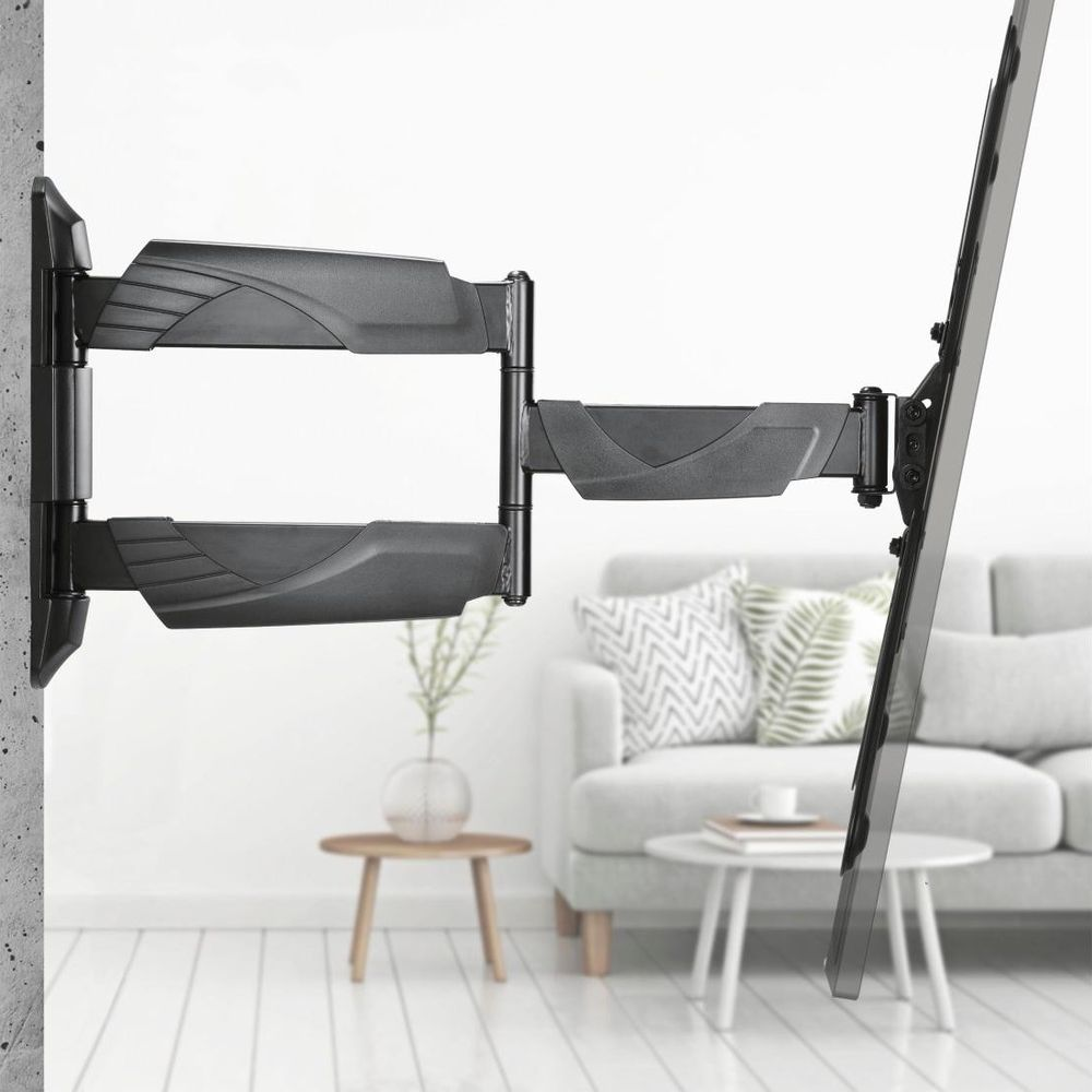 Un soporte de pared negro y extensible para TV está fijado a una pared, con una sala luminosa y borrosa al fondo.