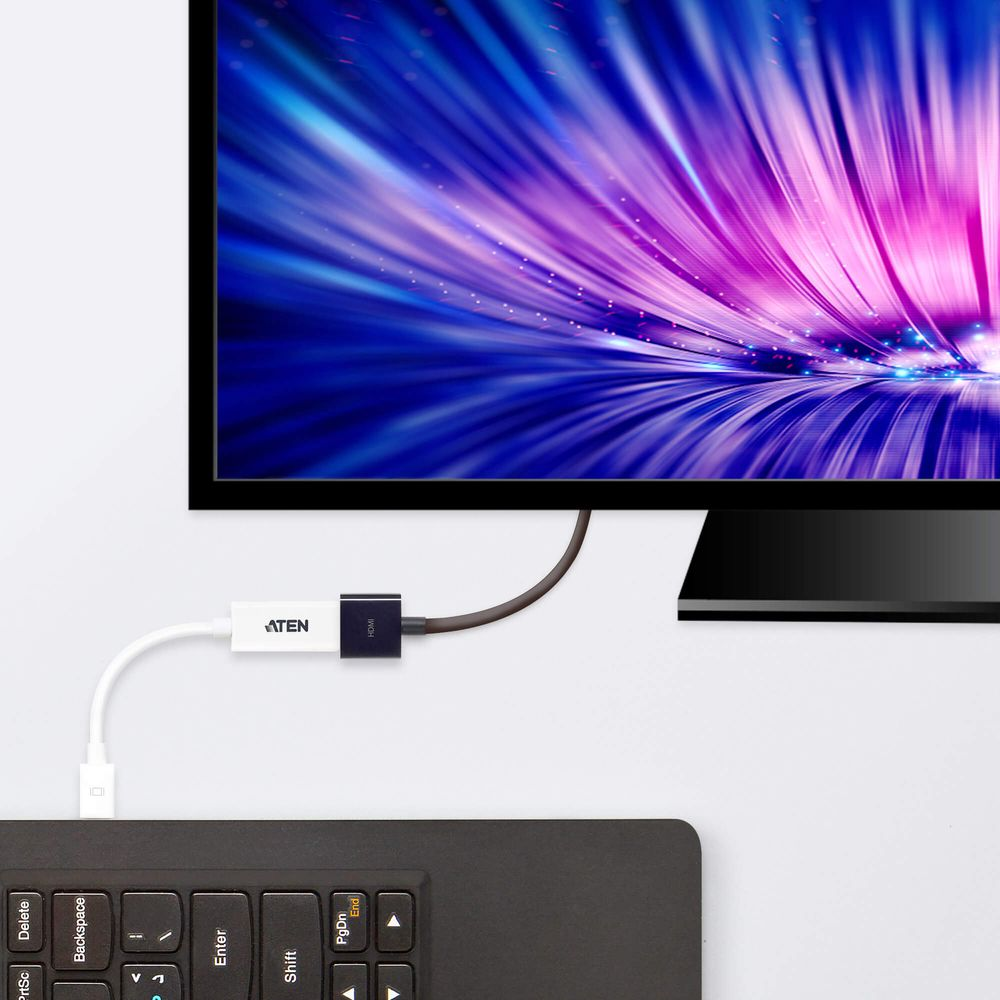 Un câble relie un clavier noir à un moniteur affichant des lignes abstraites bleues et violettes.