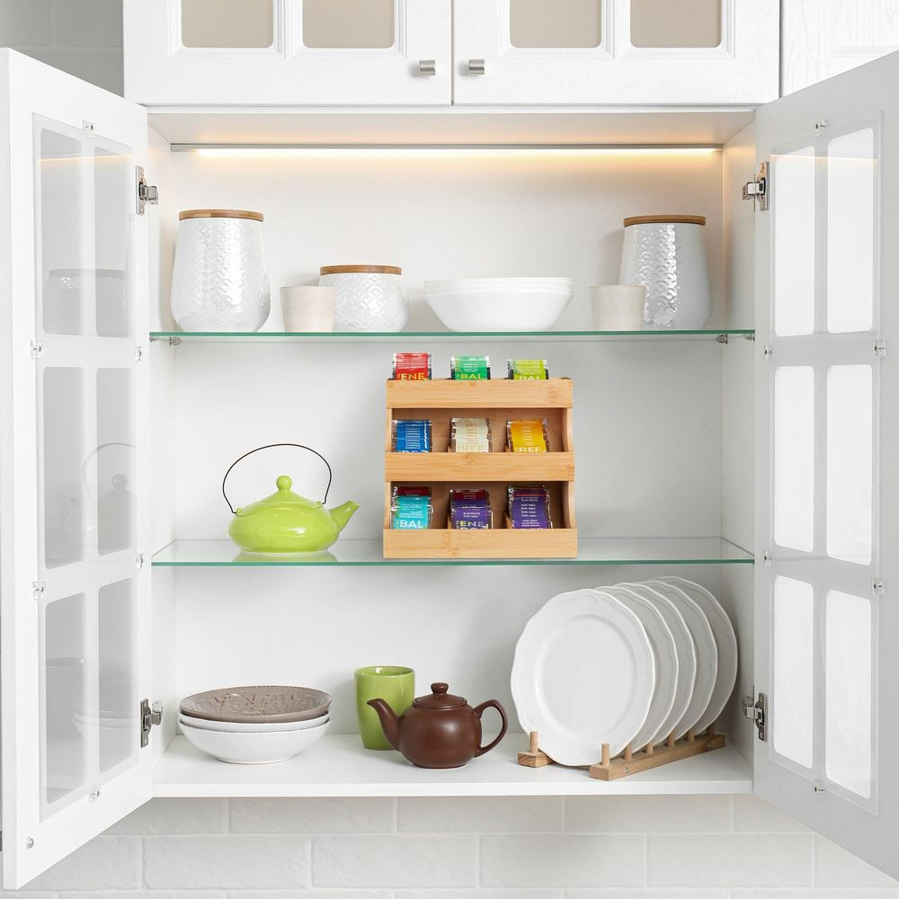 Offener weißer Schrank mit Regalen, Teedosen, Kannen, Geschirr und einem Teetablar.