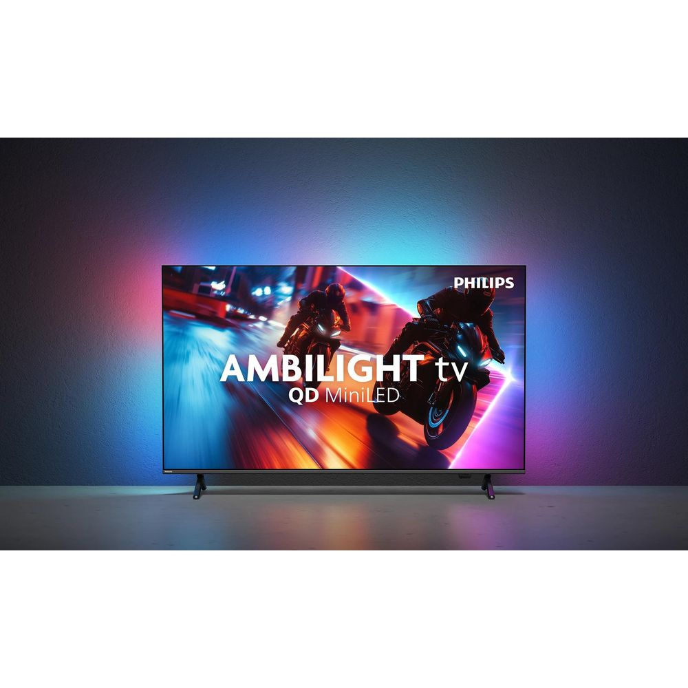 Una TV Philips Ambilight QD MiniLED mostra una gara di moto, proiettando luce colorata sulla parete.