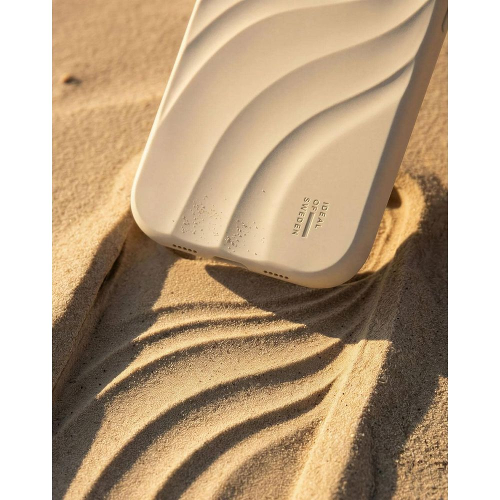 Una custodia per telefono beige con motivo a onde poggia su sabbia al sole.