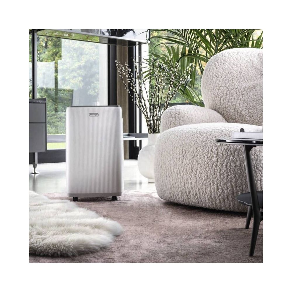 Un aire acondicionado portátil blanco en una sala moderna junto a un sillón esponjoso y plantas.