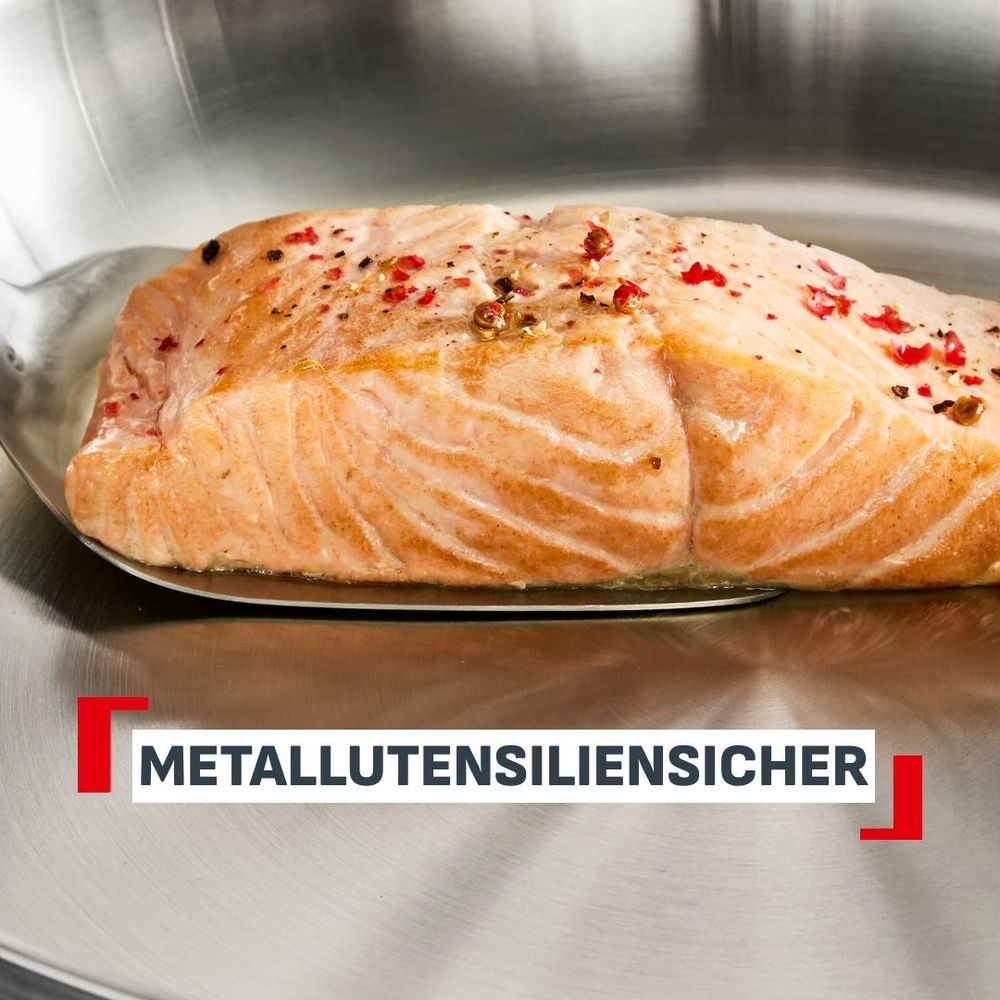 Un filete de salmón descansa sobre una espátula de metal en una sartén. Texto: METALLUTENSIENSICHER.