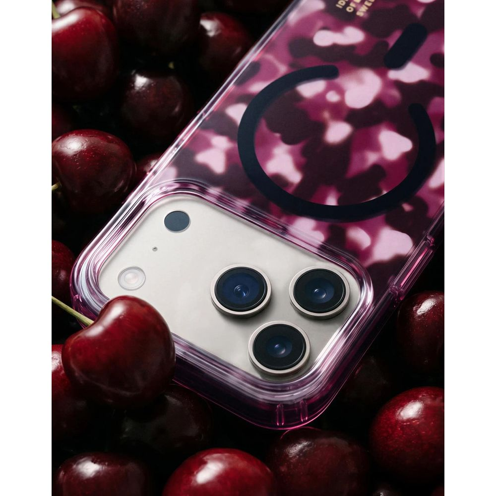 Uno smartphone rosa in una cover camouflage rosa circondato da ciliegie mature.