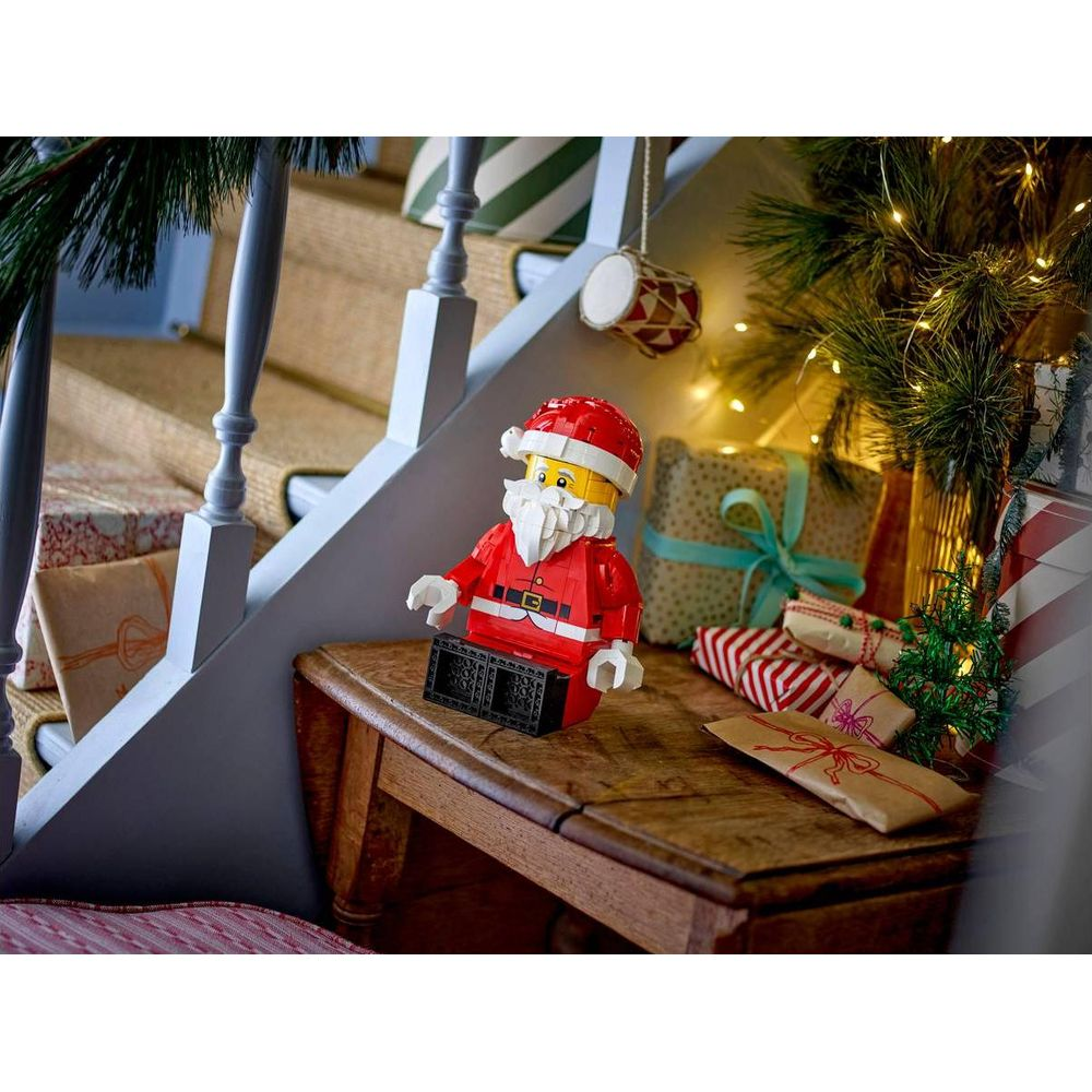 Una figura de Papá Noel de Lego está sentada en una mesa de madera cerca de regalos.