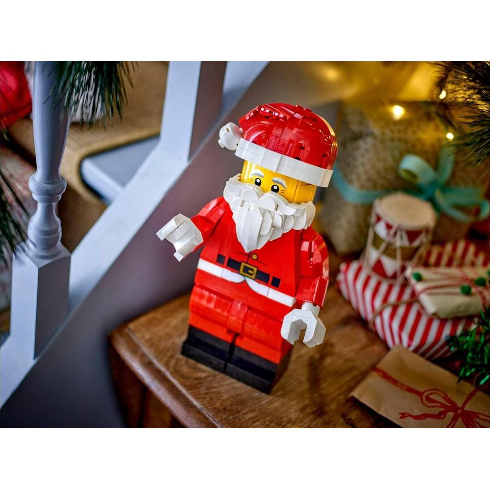 Una figura de Papá Noel de Lego sobre una mesa de madera con regalos de fondo.