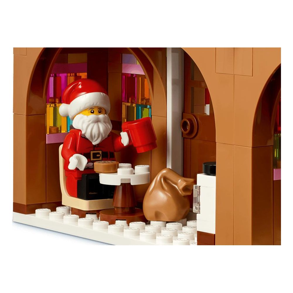 Papá Noel de Lego sentado en una mesa pequeña con taza roja, y un saco marrón al lado.