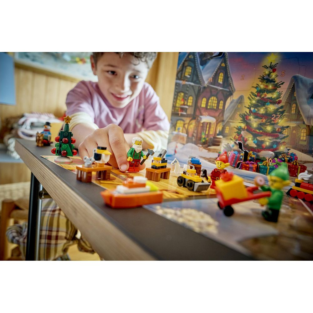 Uśmiechnięty chłopiec ustawia figurki świąteczne Lego przed kalendarzem adwentowym.