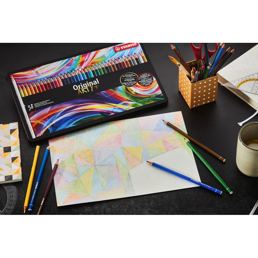 Bunte Stifte, Malpapier, Stiftehalter und eine Schachtel mit Buntstiften auf schwarzem Tisch.