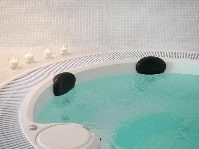 Un jacuzzi blanco redondo lleno de agua turquesa, con reposacabezas negros y velas encendidas al fondo.
