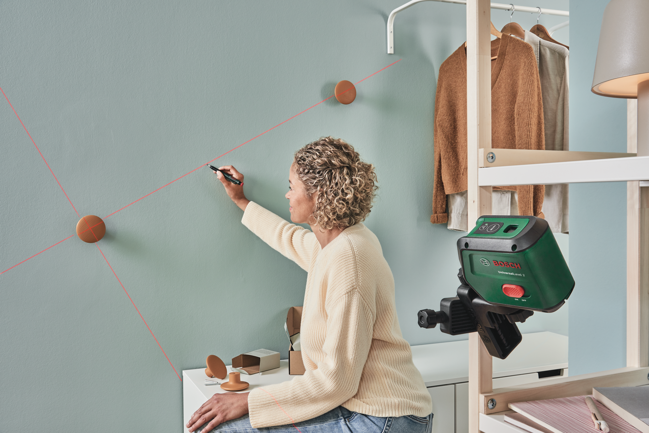 Eine Frau markiert mit einem Stift eine Wand anhand roter Laserlinien, die von einem Bosch-Lasergerät projiziert werden.