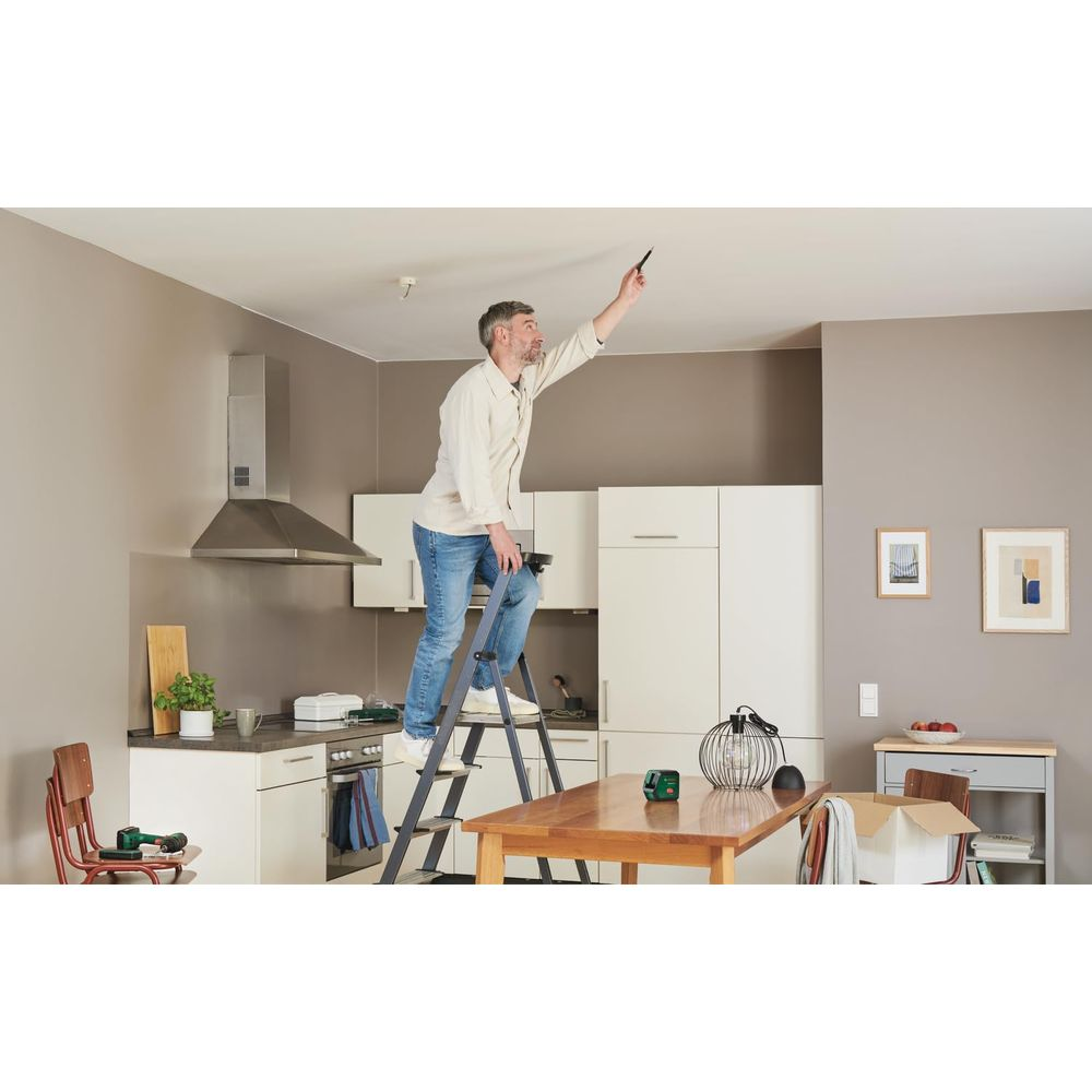 Ein Mann auf einer Leiter in einer Küche zeigt an die Decke.