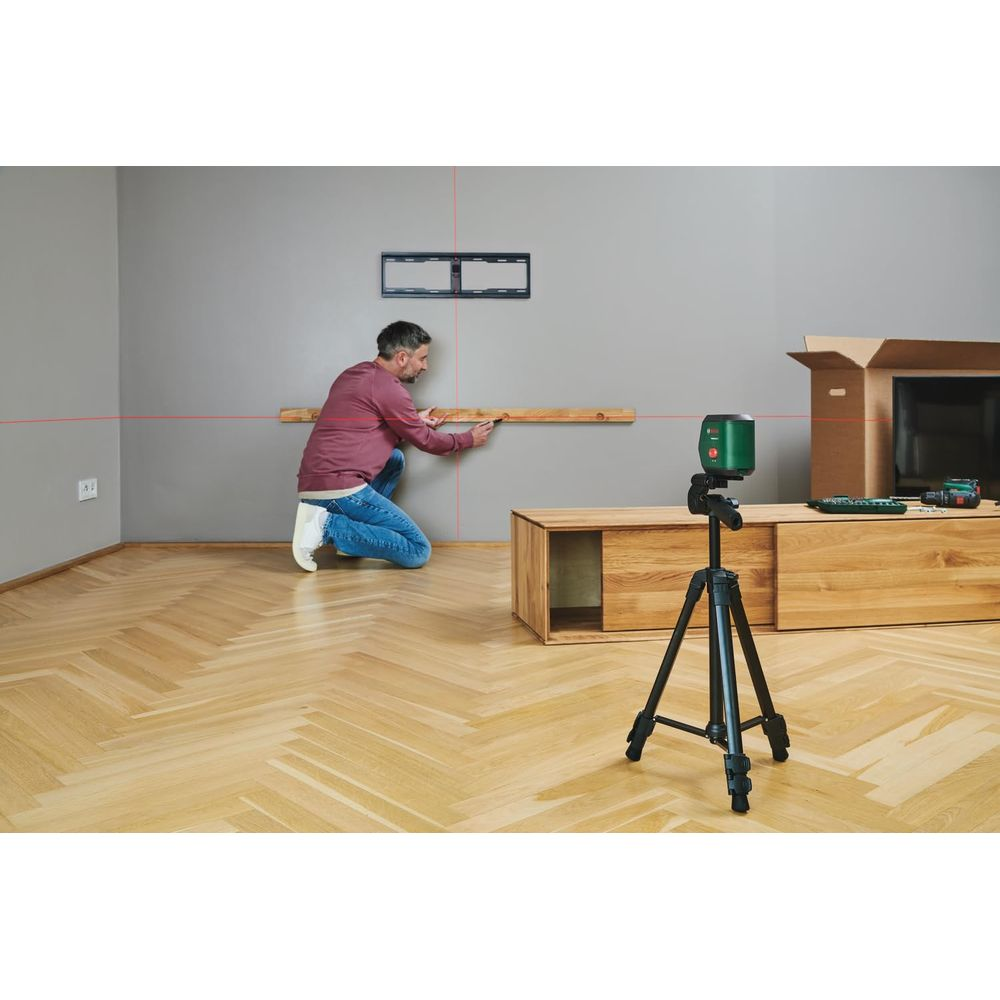 Ein Mann kniet auf Parkettboden und markiert eine Holzleiste, die von einem roten Laserstrahl ausgerichtet wird.