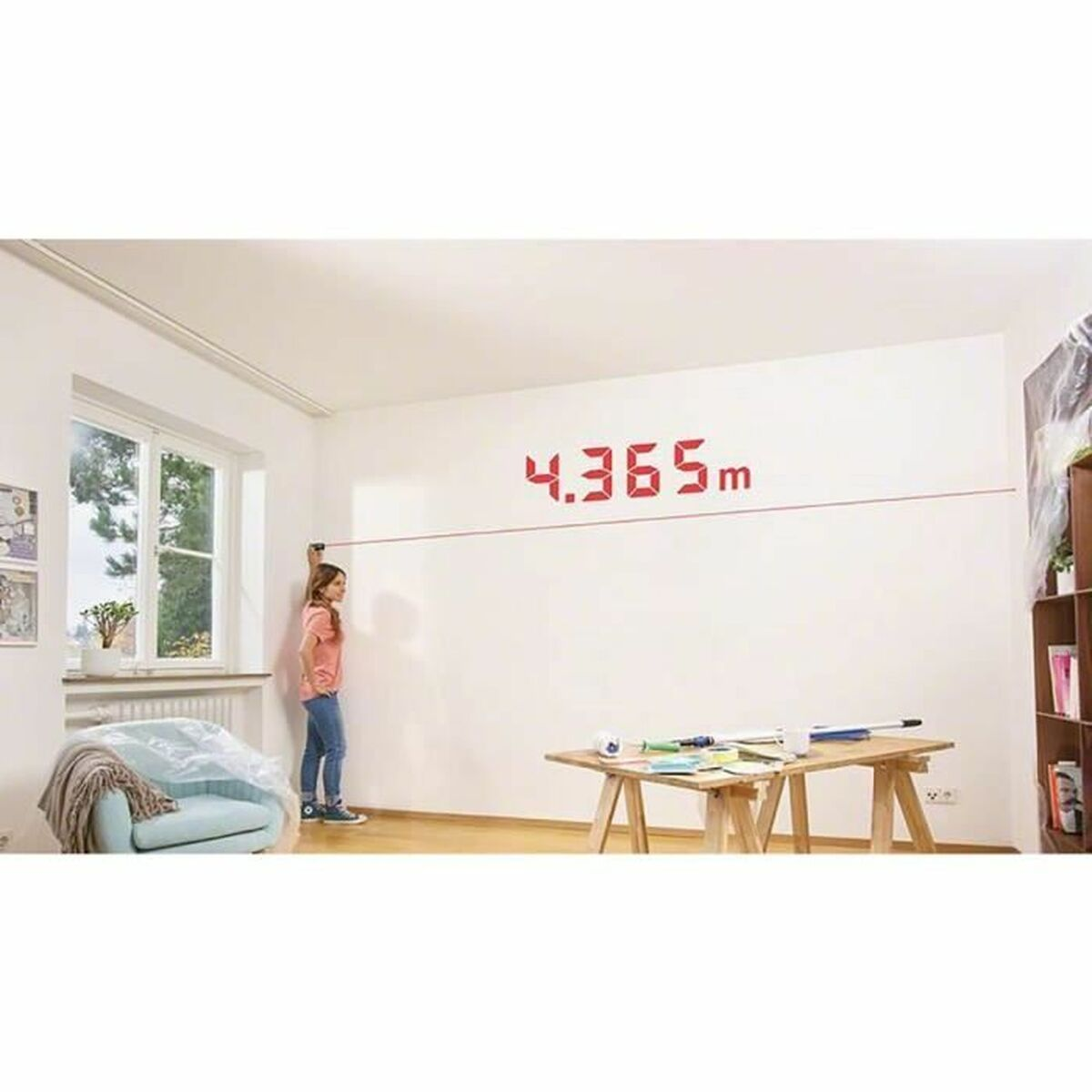 Eine Frau misst eine Wand mit einem Lasergerät, wobei die Messung als rote Ziffern auf der Wand angezeigt wird.