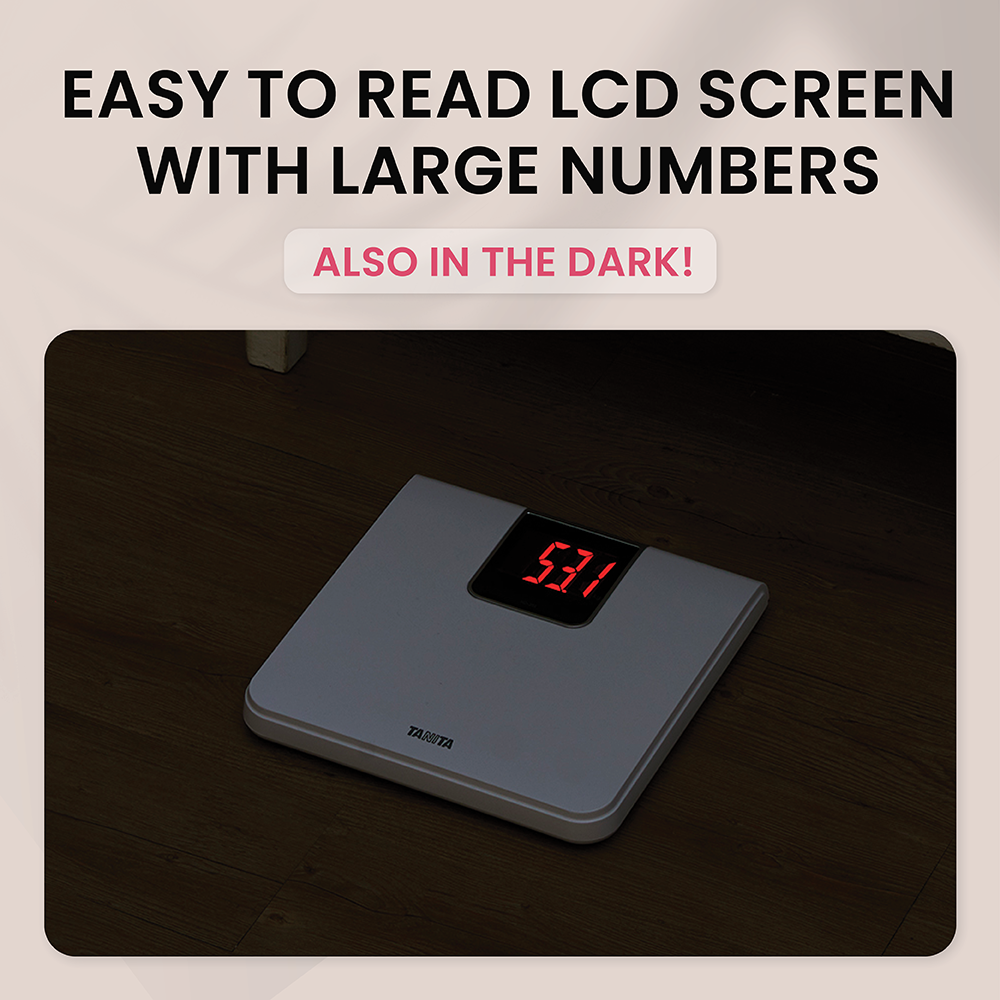 A white digital scale with lit red LCD screen on a dark wooden floor, with text above about easy to read numbers.