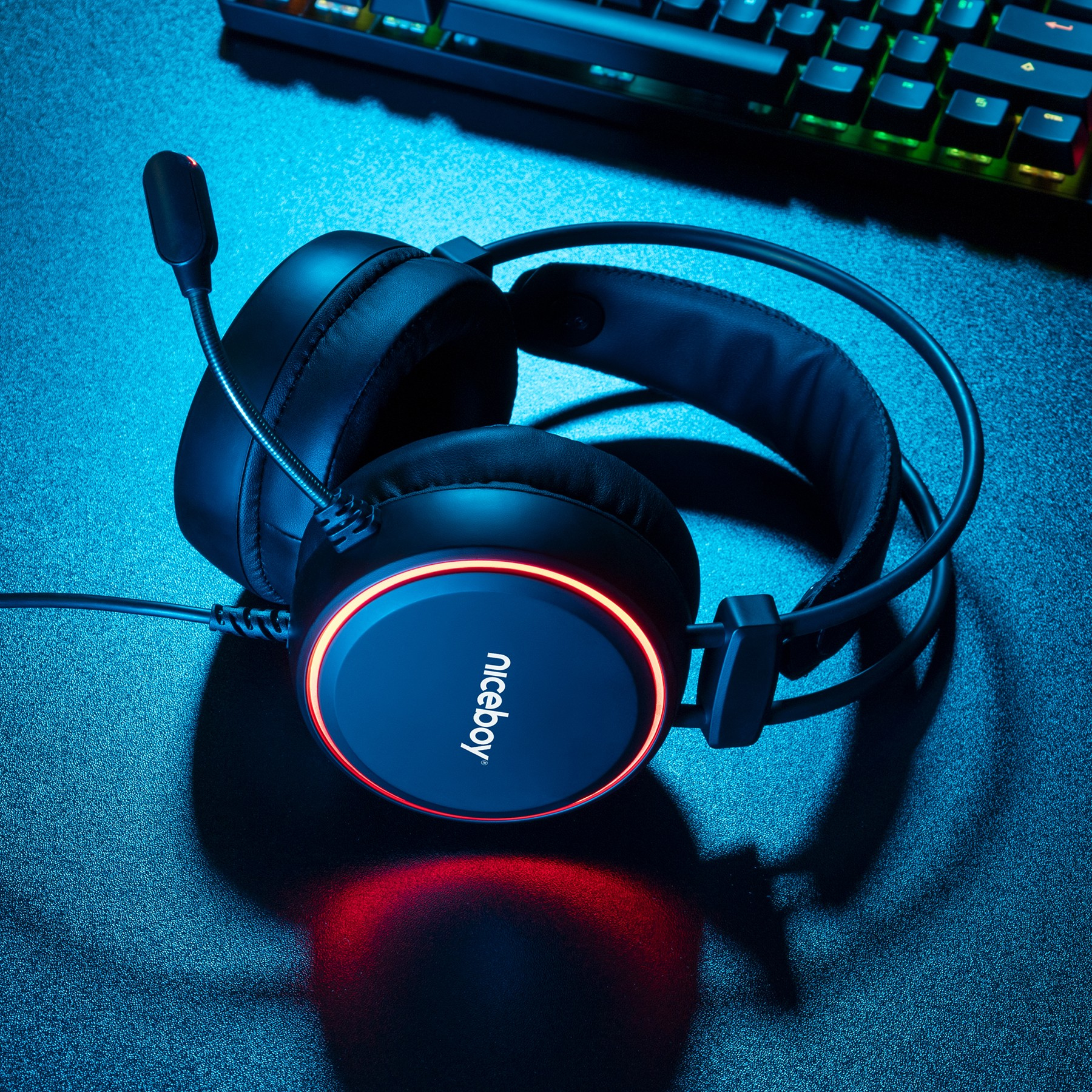 Schwarzes Gaming-Headset mit leuchtend rotem Ring und Mikrofon liegt auf blauem Schreibtisch.