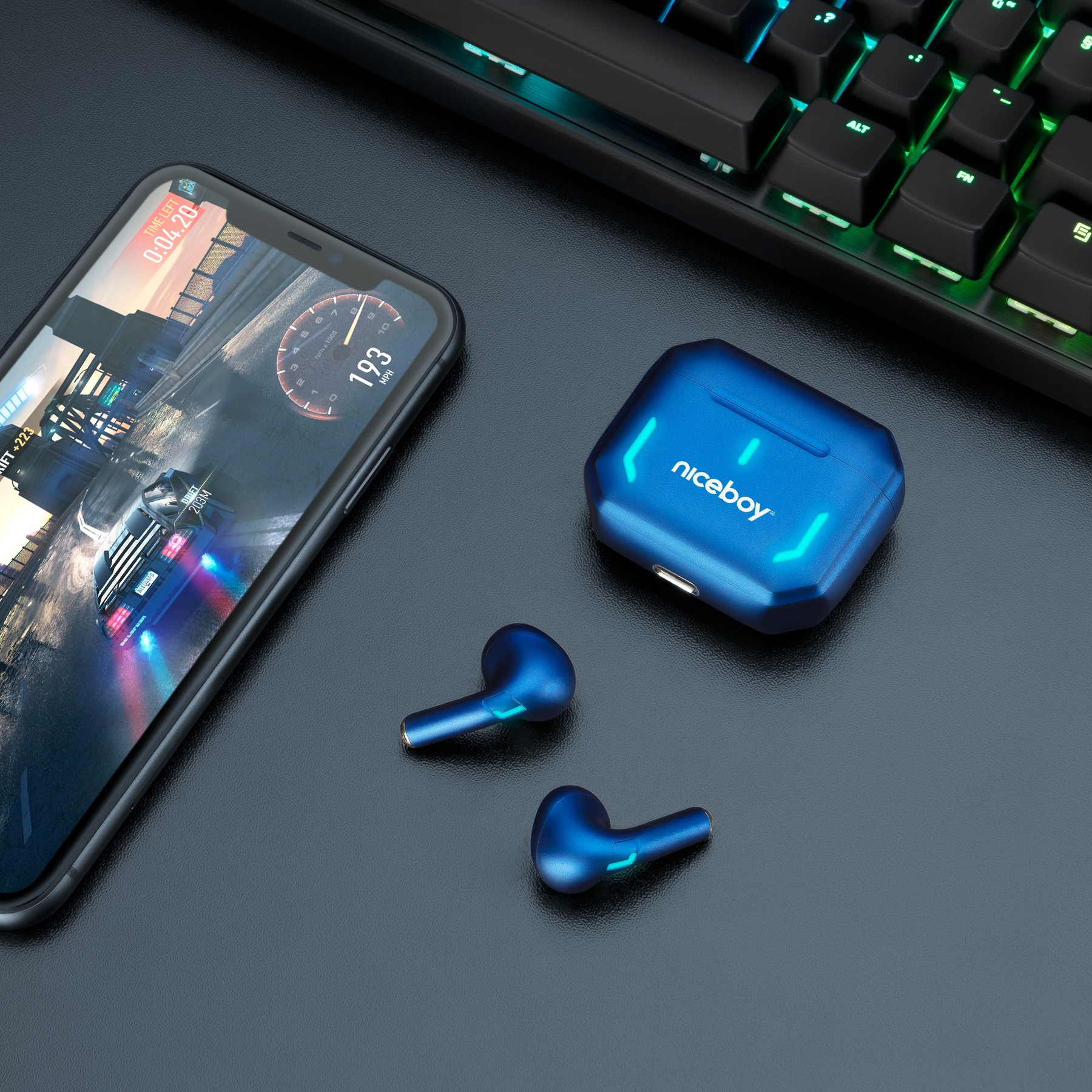 Blaue kabellose Ohrhörer mit Ladecase, ein Smartphone mit Rennspiel und eine RGB-Tastatur auf schwarzem Tisch.