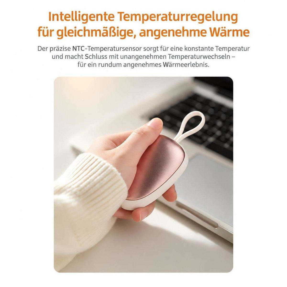 Hand hält ein kleines rosa Handwärmegerät mit einer Schlaufe vor einem Laptop.