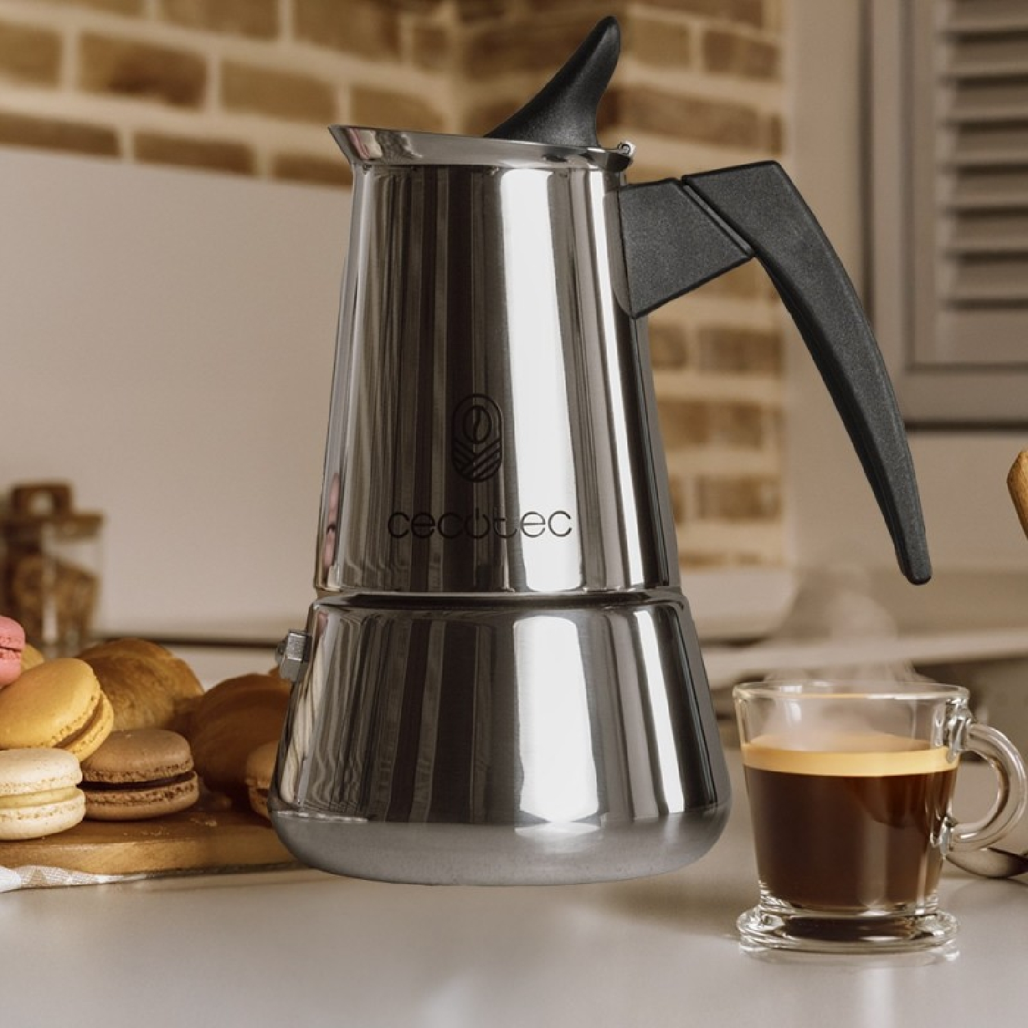 Una brillante cafetera moka de acero inoxidable se encuentra en una encimera junto a una taza de espresso humeante.