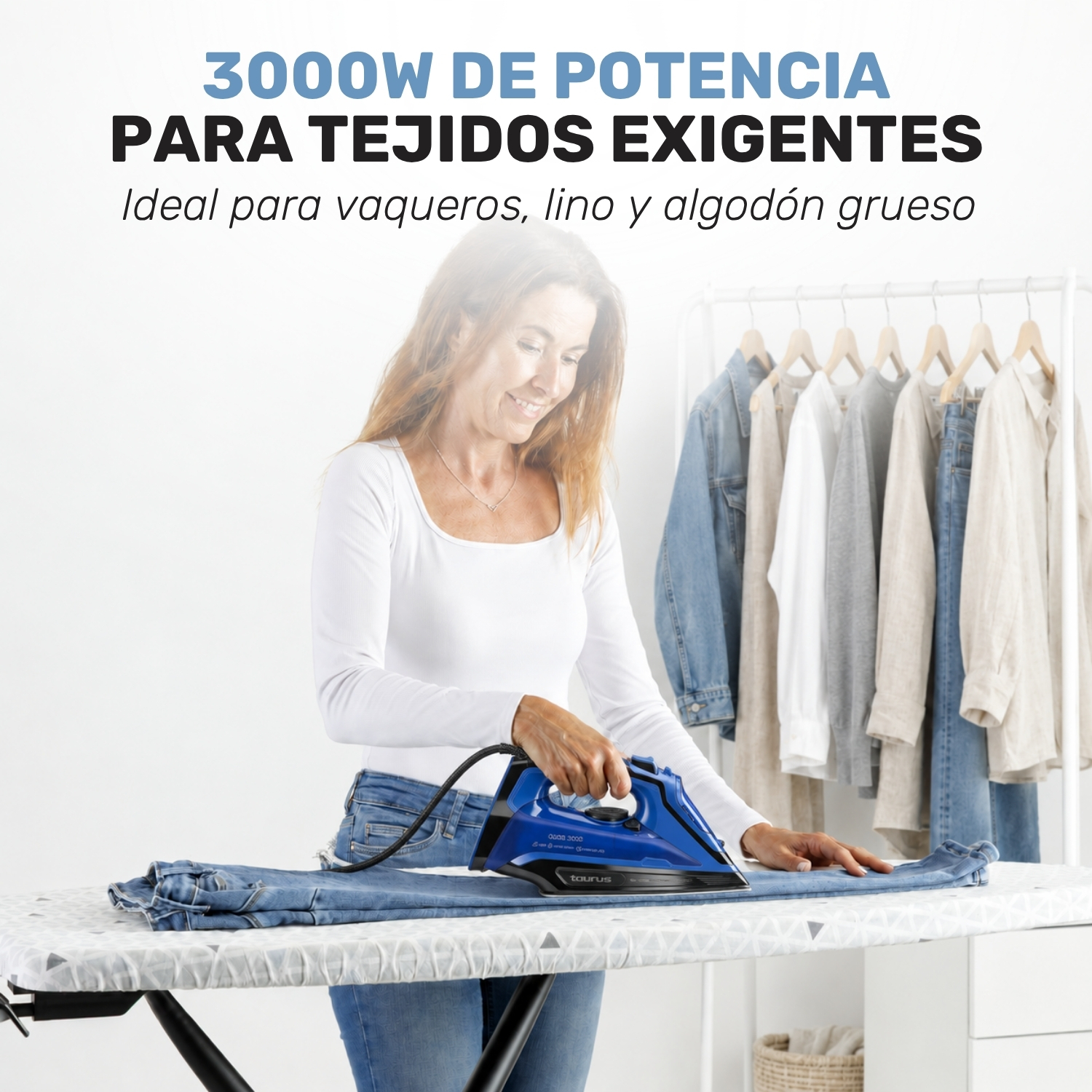 Una mujer plancha vaqueros en una tabla de planchar con ropa colgada al fondo.