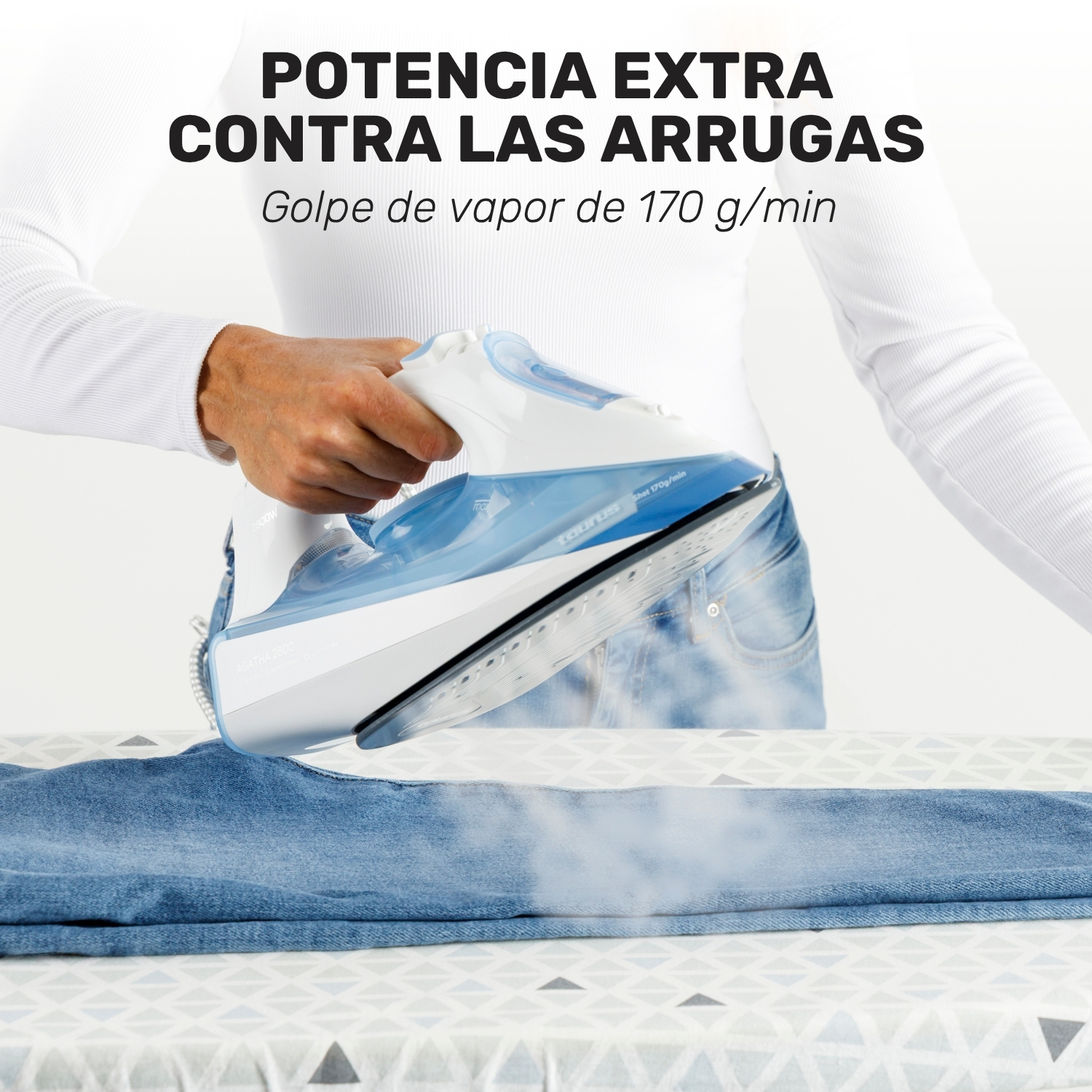 Una persona sostiene una plancha blanca y azul lanzando vapor sobre unos vaqueros en una tabla de planchar.