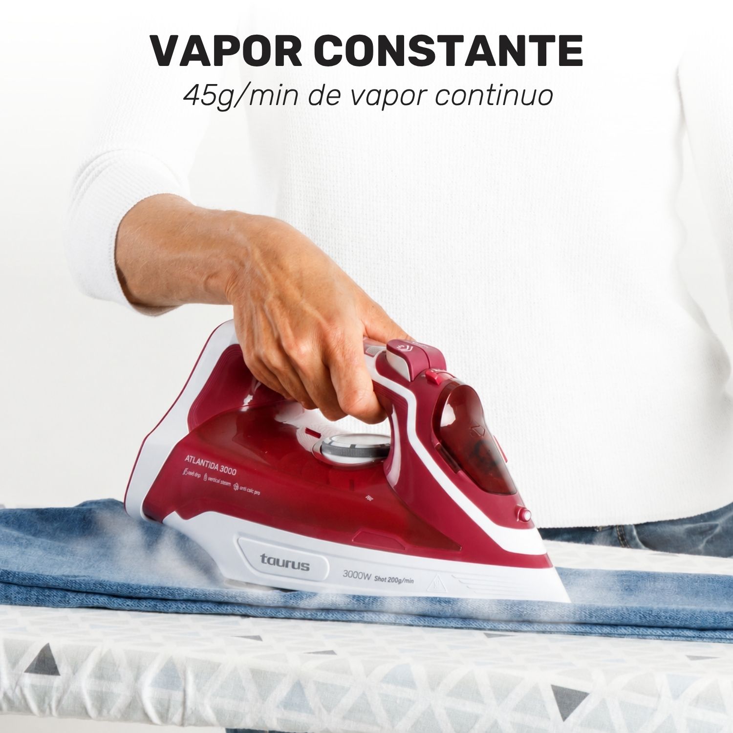 Una mano plancha vaqueros azules con una plancha de vapor roja Taurus, mientras sale vapor.