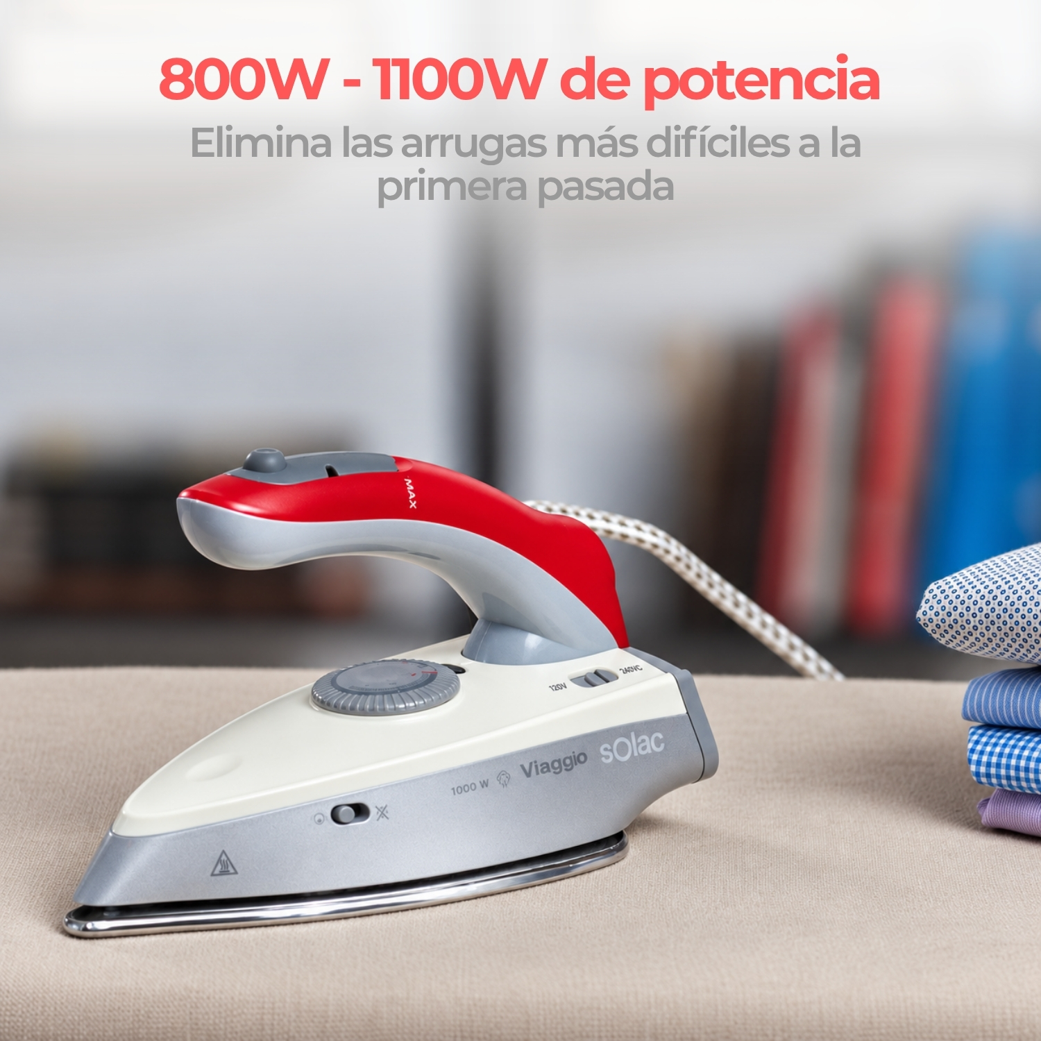 Una plancha de viaje roja y blanca sobre una tabla de planchar junto a ropa doblada.